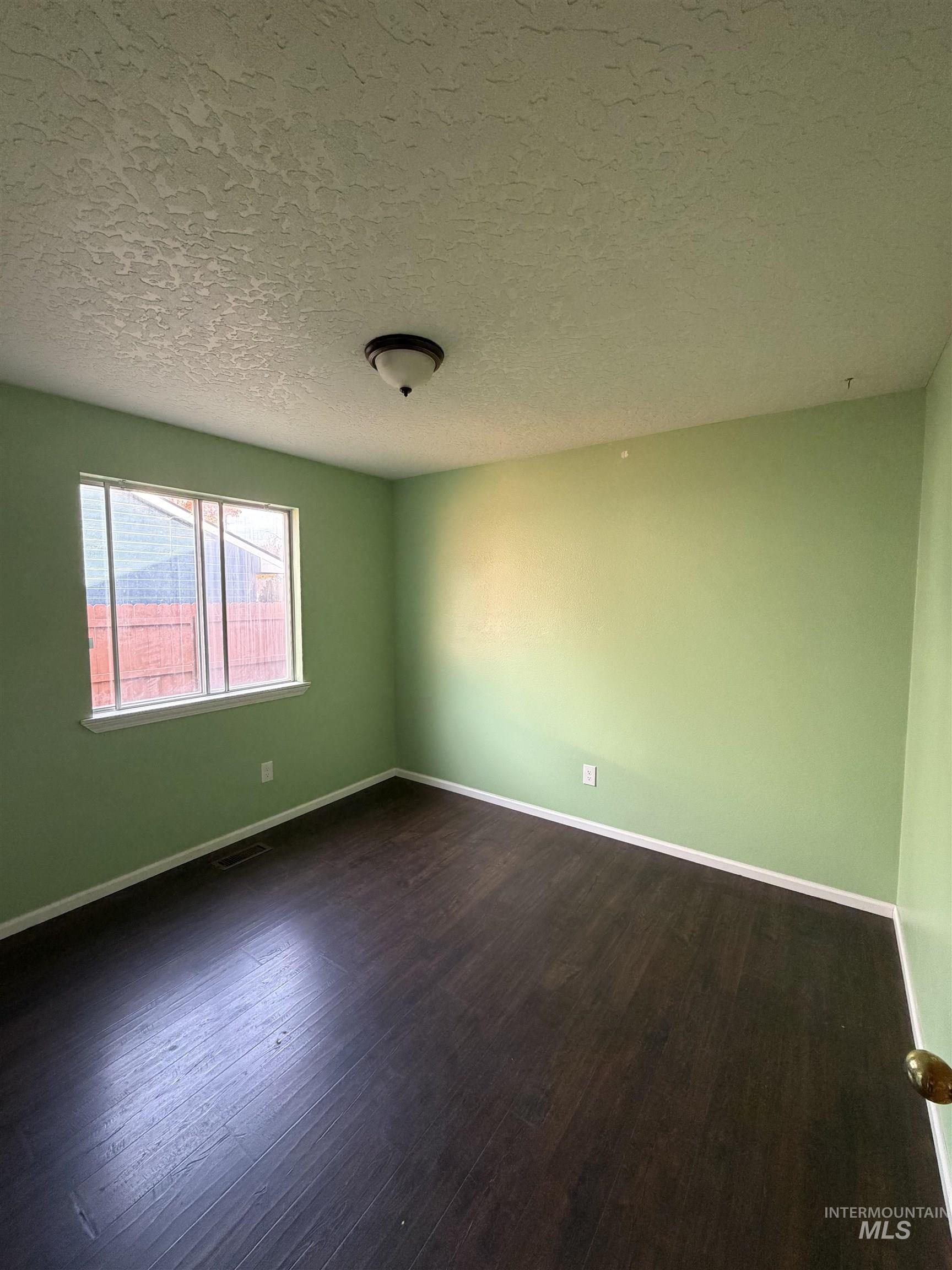 Spare room featuring dark wood-style flooring and a textured ceiling