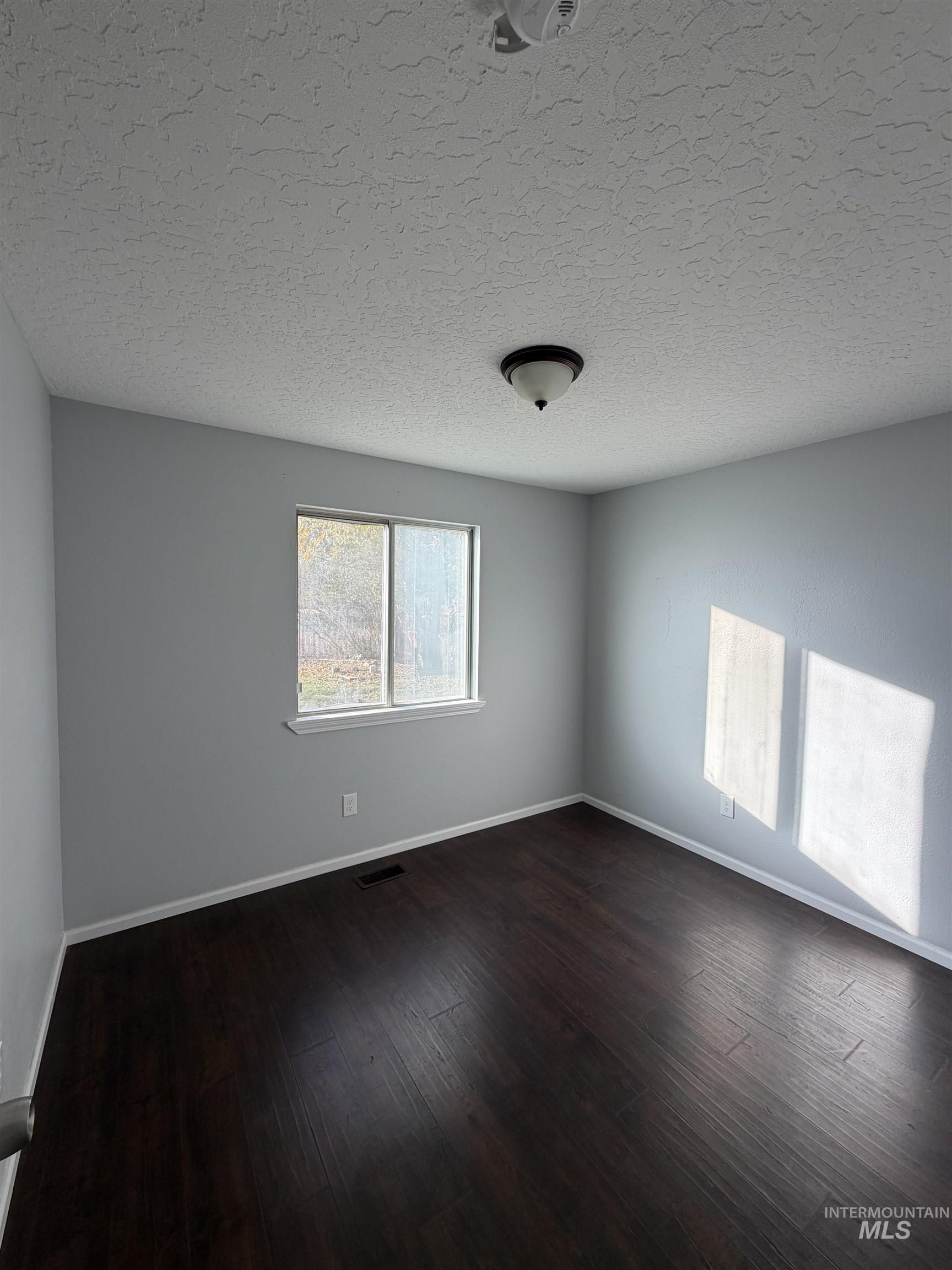 Empty room featuring dark wood-type flooring and a textured ceiling