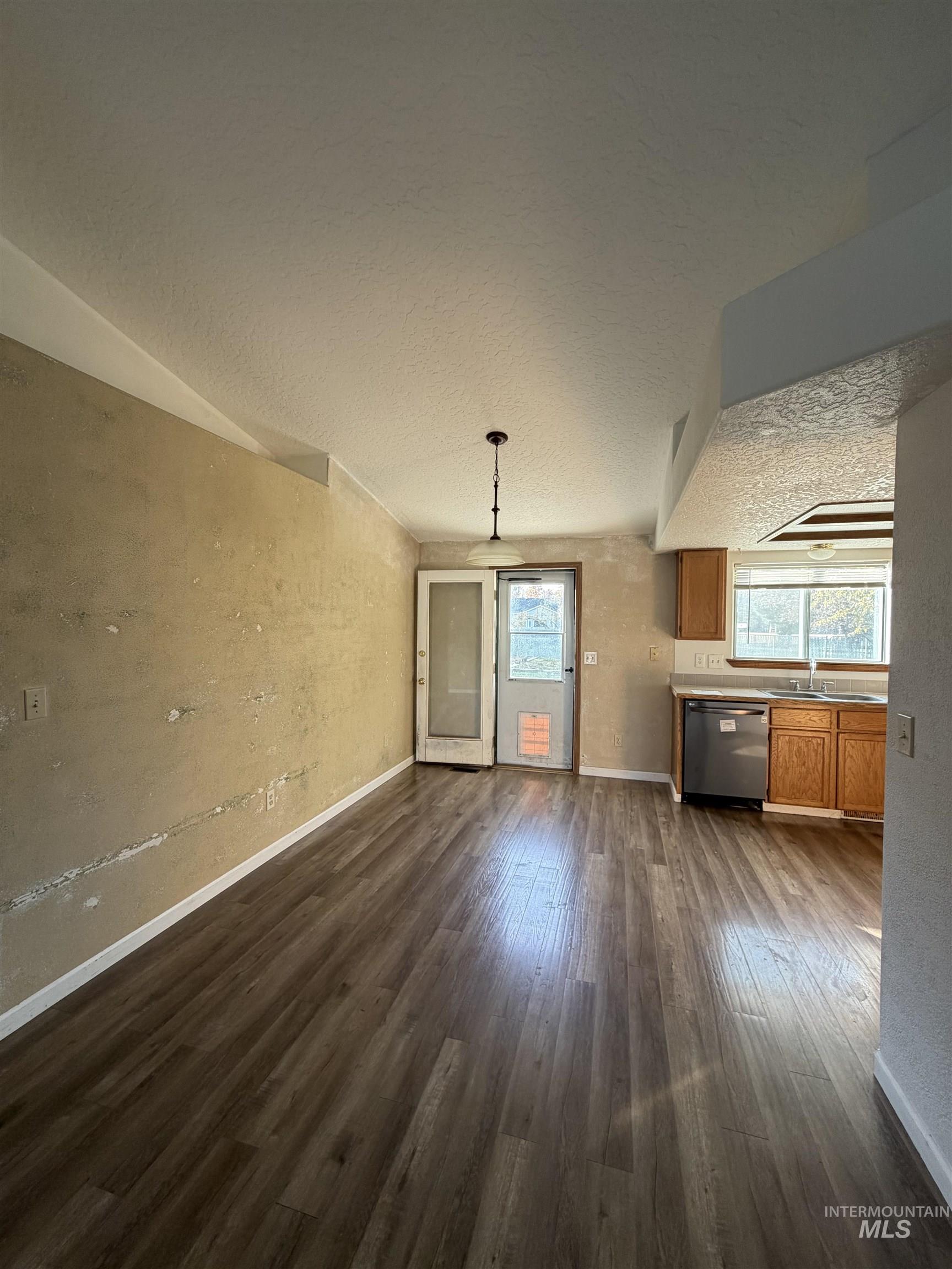 Unfurnished living room featuring a textured ceiling, dark wood-type flooring, and a textured wall