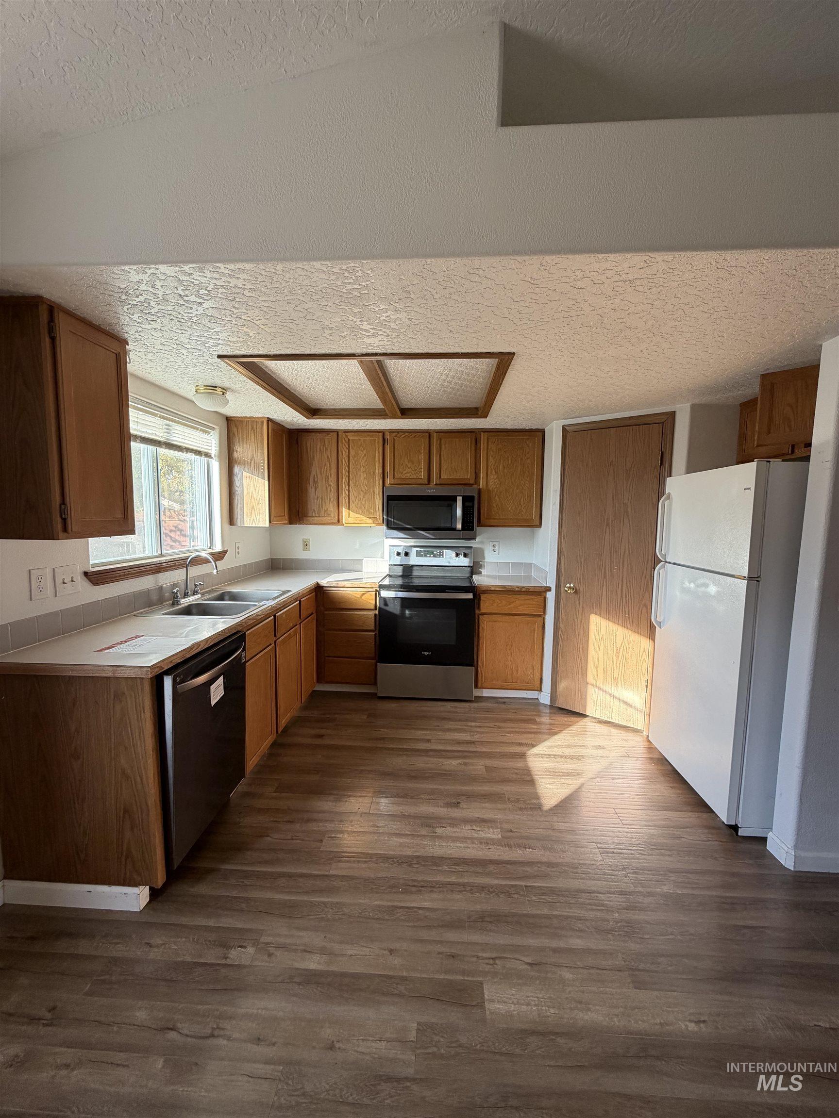 Kitchen with a textured ceiling, stainless steel appliances, dark wood-style floors, and brown cabinets
