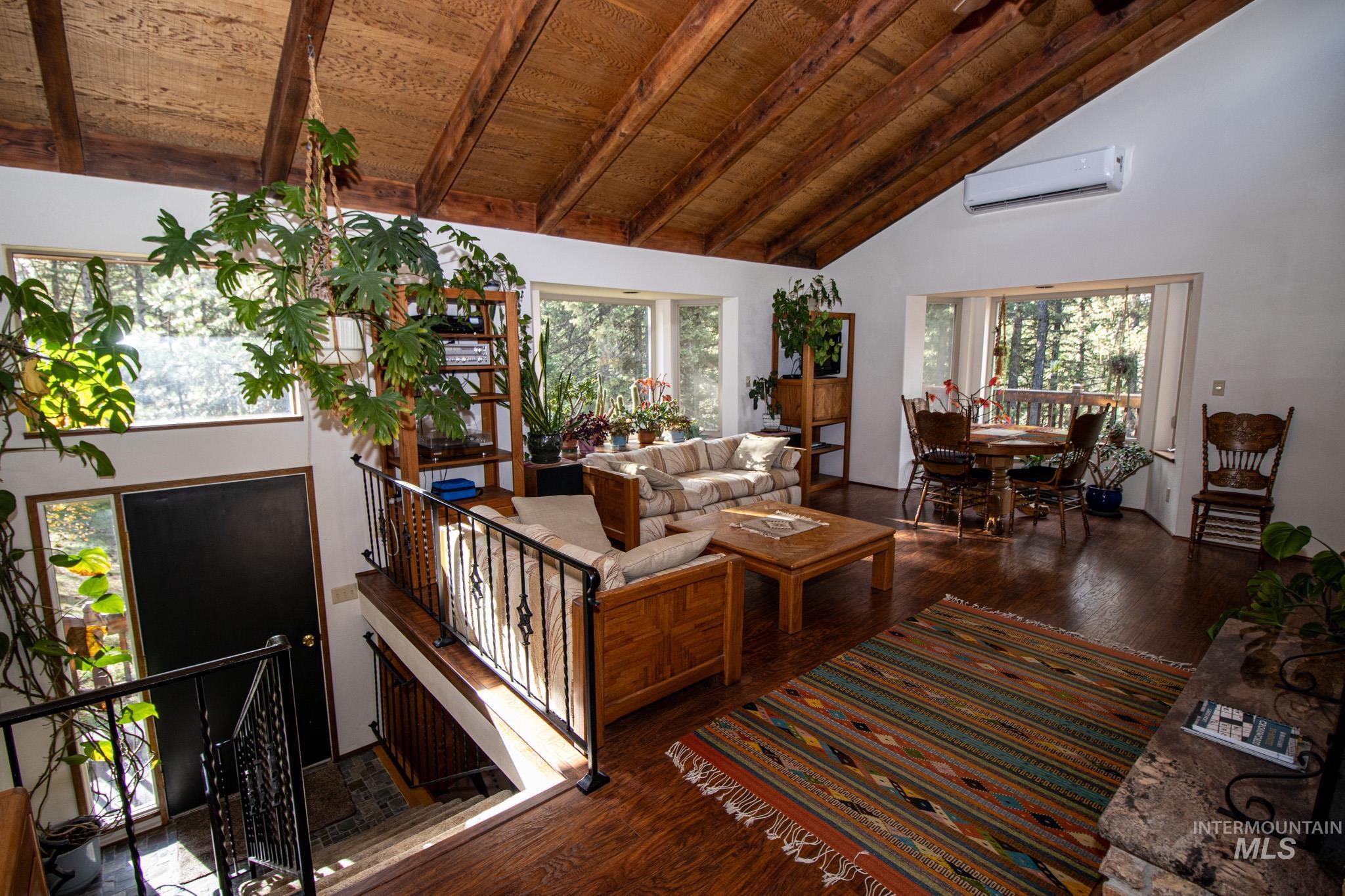 Living area with wood finished floors, high vaulted ceiling, a wood ceiling with exposed beams, and a wall mounted AC