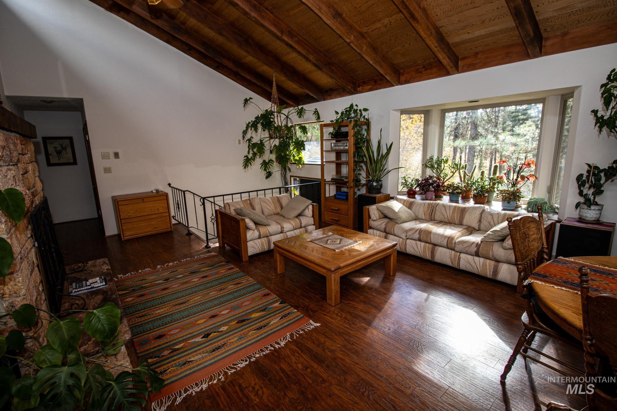 Living room featuring wood-type flooring, a wooden ceiling with exposed beams, a stone fireplace, and high vaulted ceiling