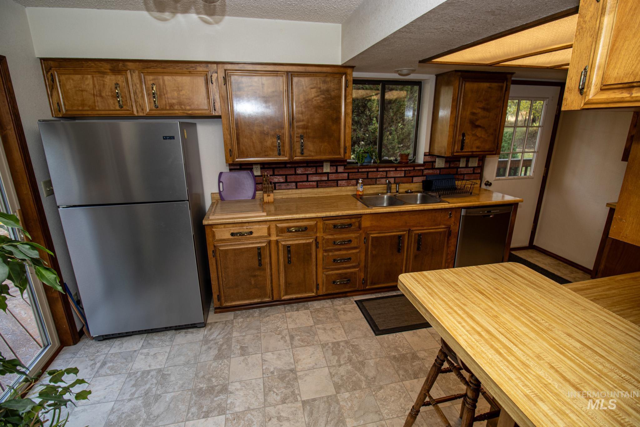 Kitchen featuring light countertops, appliances with stainless steel finishes, backsplash, stone finish floors, and a textured ceiling