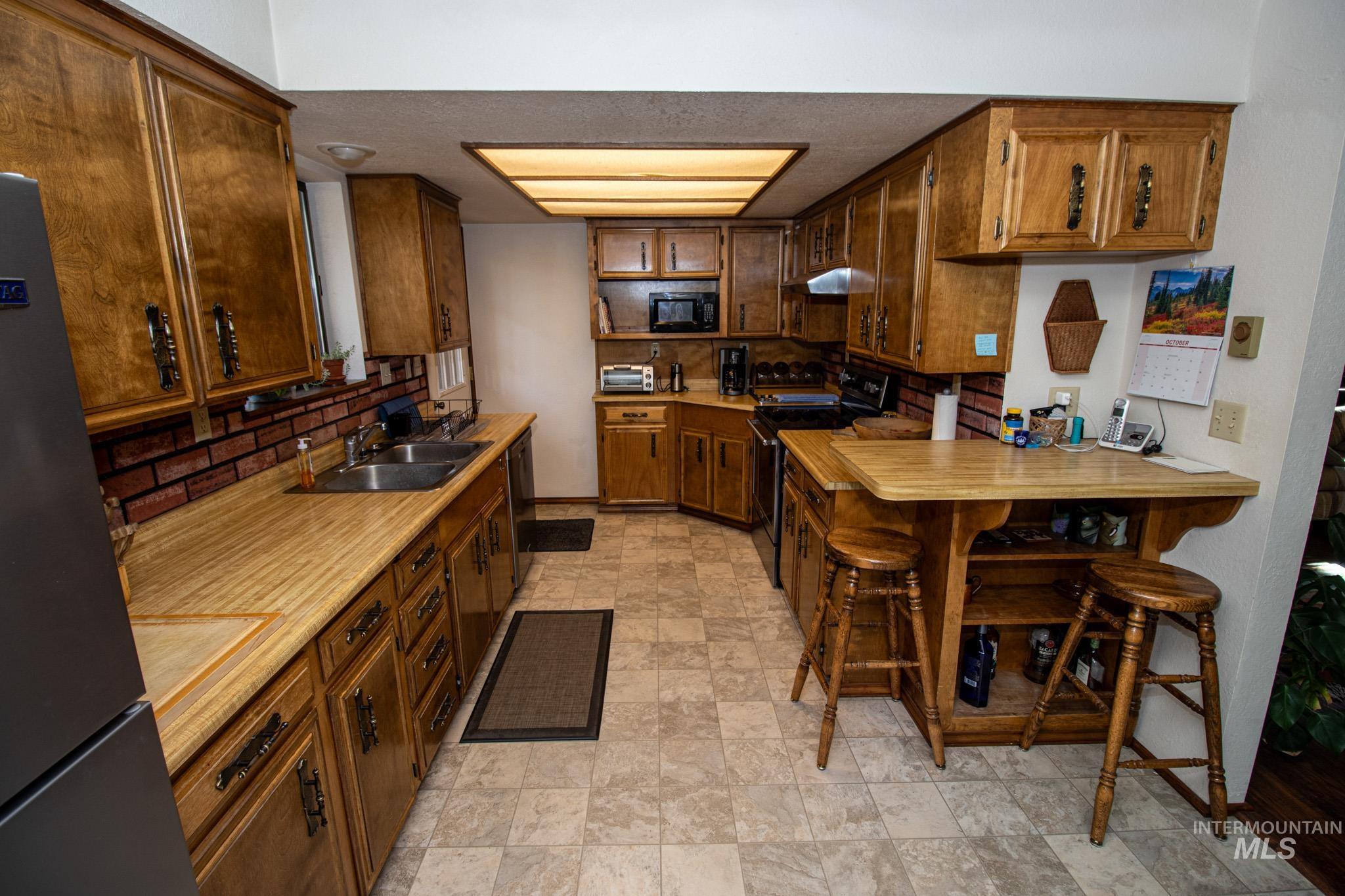 Kitchen featuring light countertops, black appliances, brown cabinetry, a peninsula, and backsplash