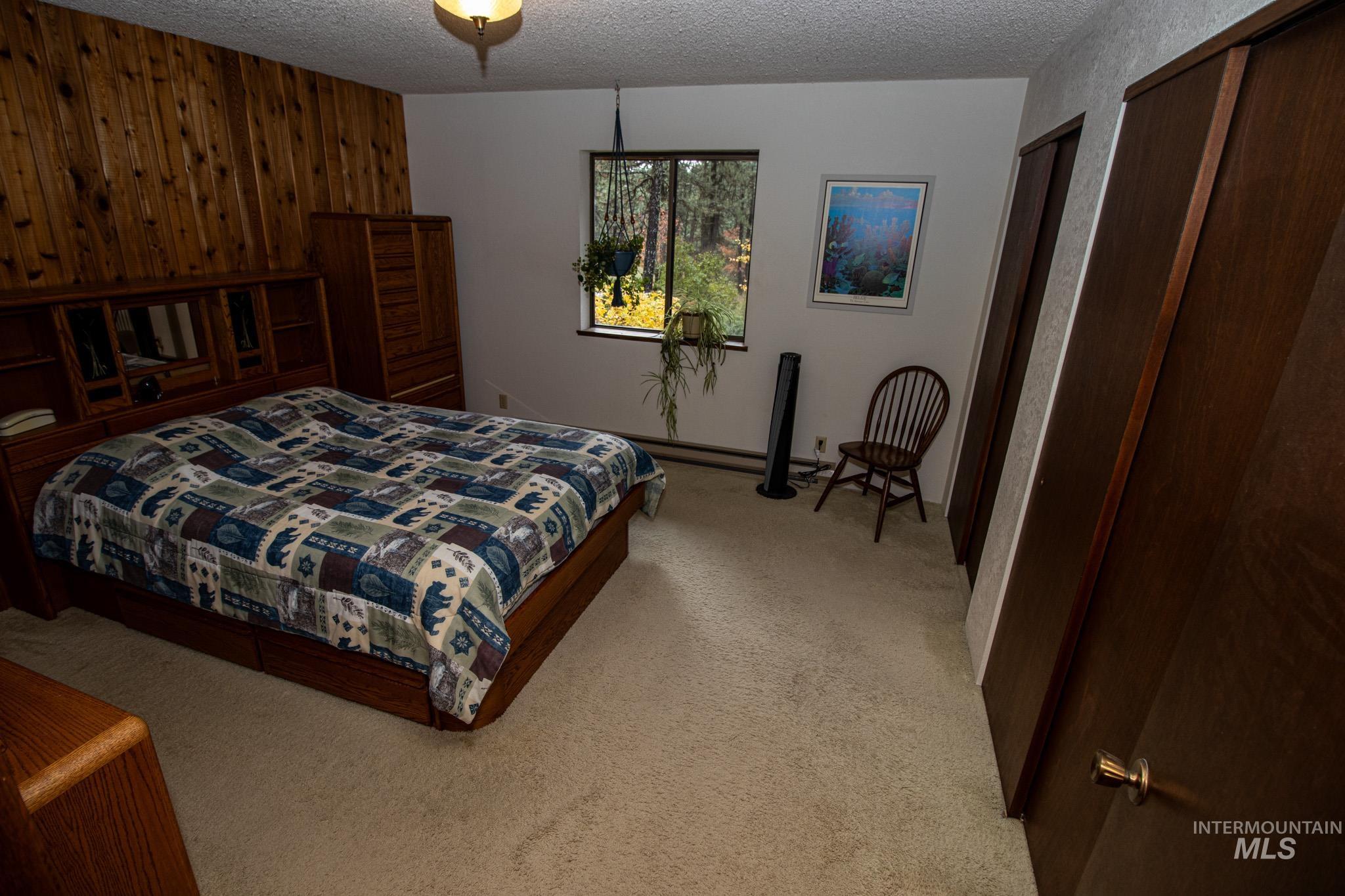 Bedroom featuring light colored carpet, a textured ceiling, wood walls, and two closets