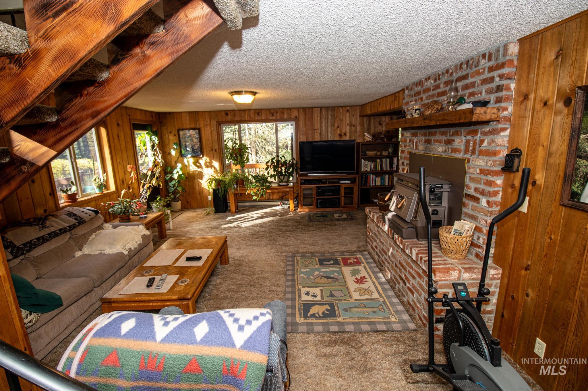 Living area featuring wooden walls, carpet, a textured ceiling, healthy amount of natural light, and a brick fireplace