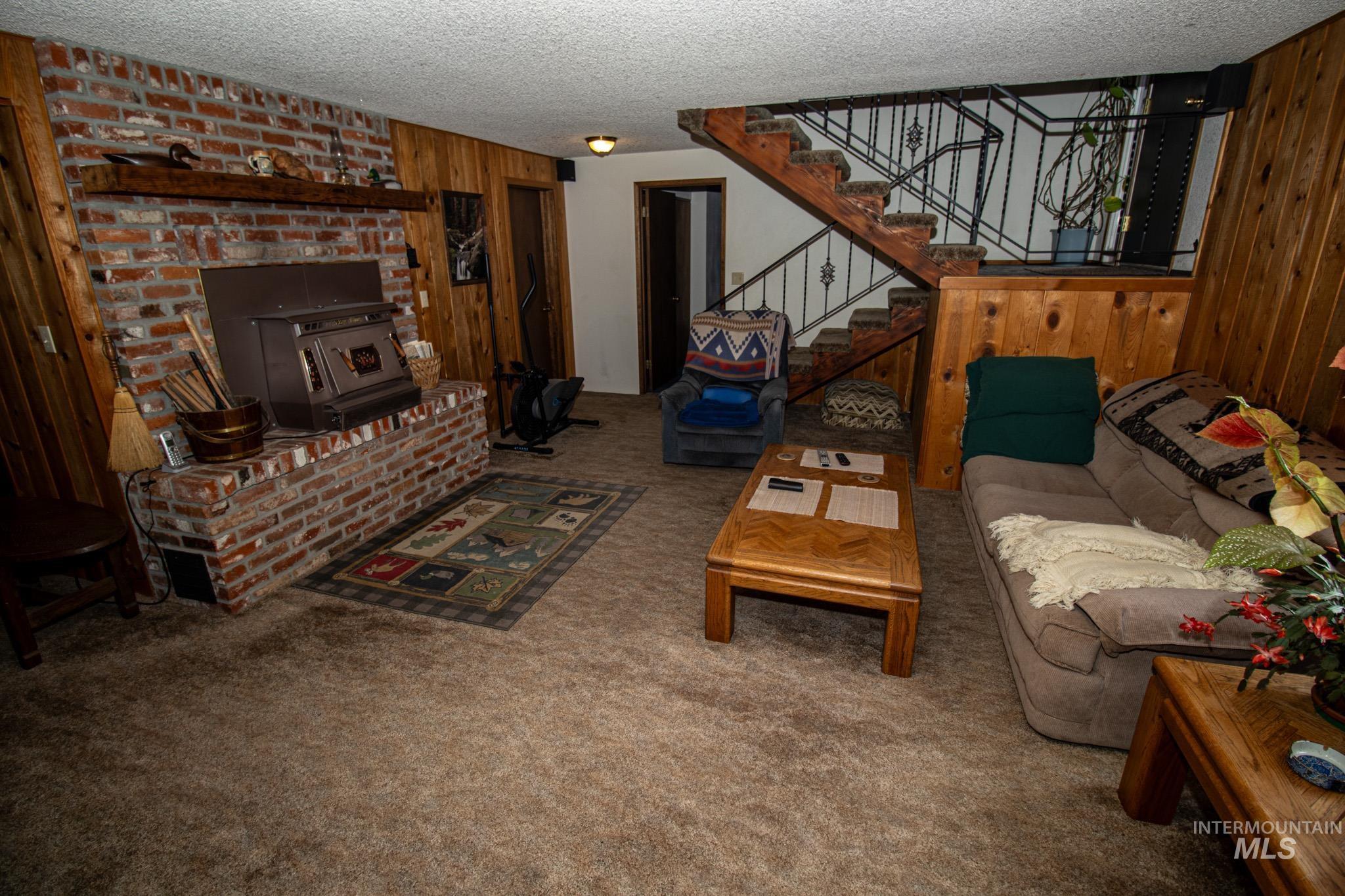 Living room featuring wooden walls, carpet floors, a wood stove, a textured ceiling, and stairs