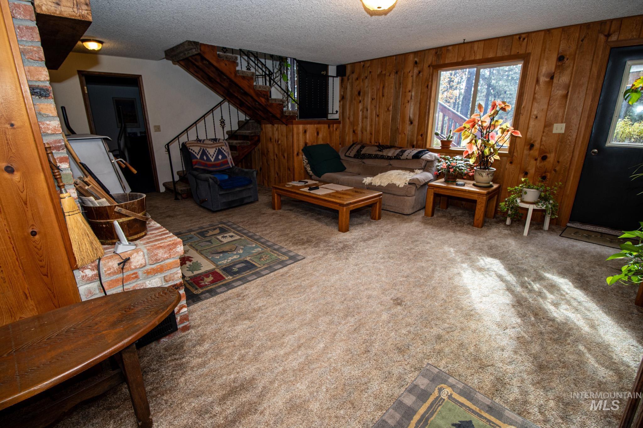 Carpeted living area with a textured ceiling, stairs, and wood walls