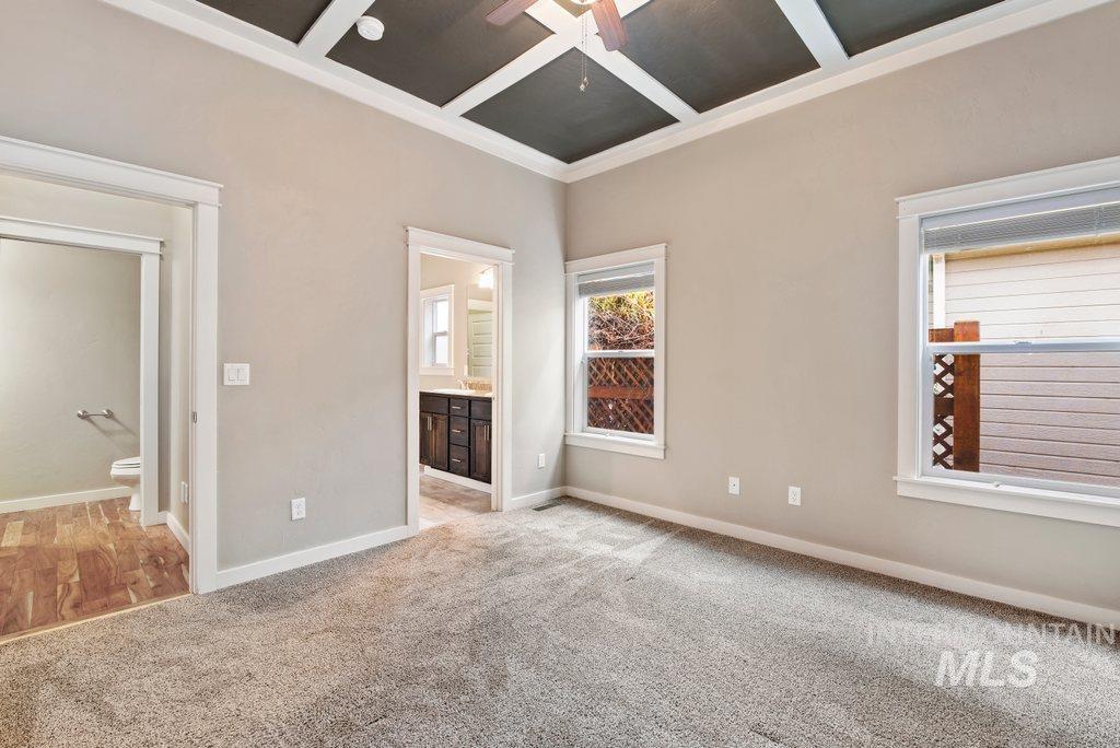 Unfurnished bedroom with coffered ceiling, connected bathroom, light carpet, ornamental molding, and ceiling fan