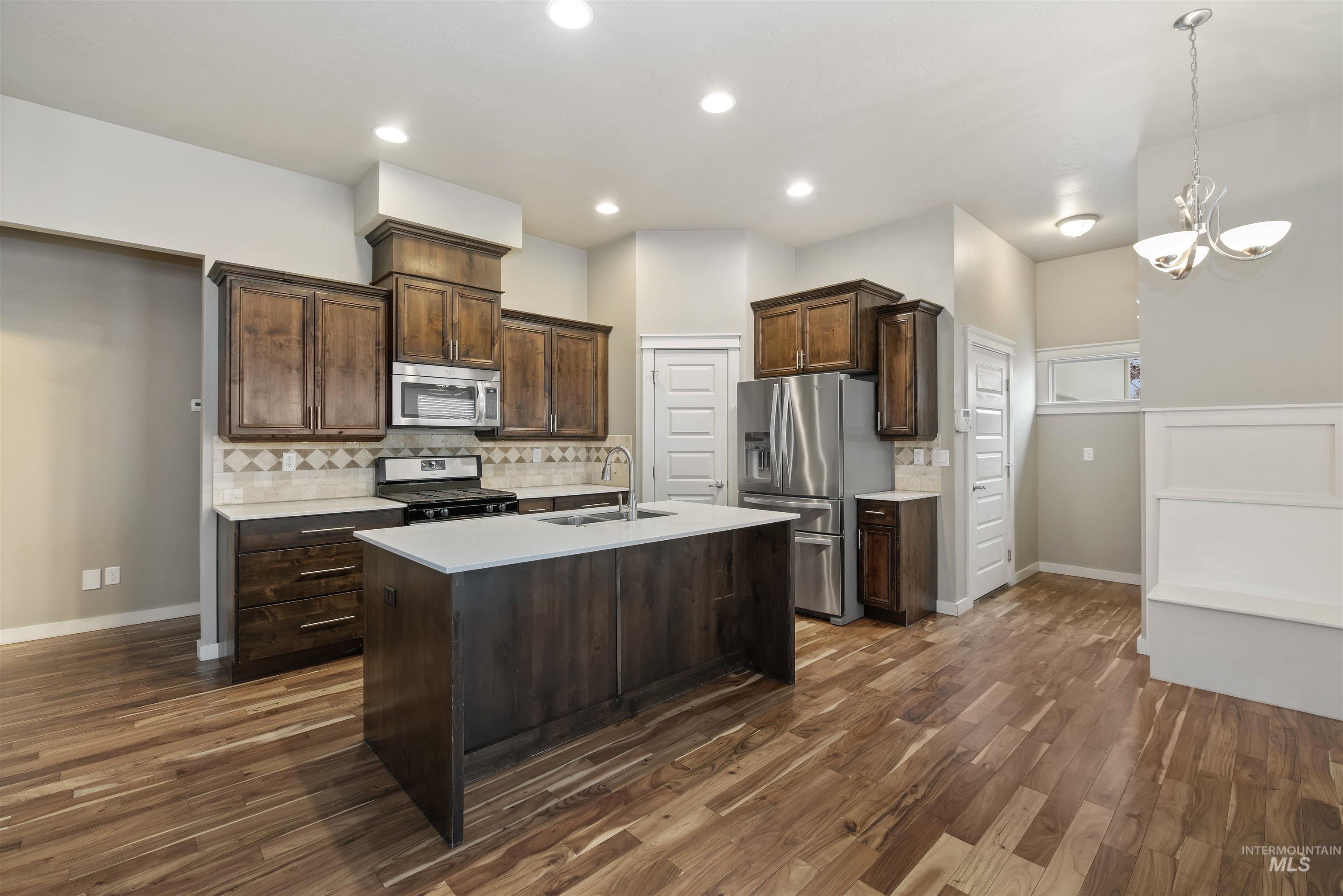 Kitchen with appliances with stainless steel finishes, tasteful backsplash, dark brown cabinetry, dark wood-type flooring, and recessed lighting