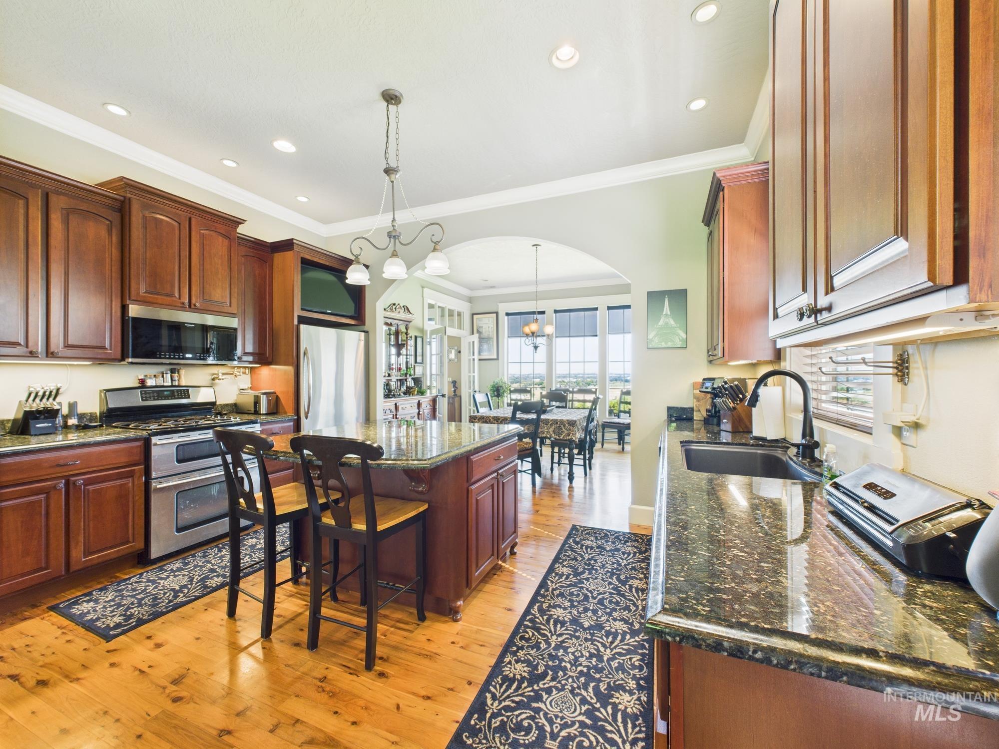 Kitchen with arched walkways, stainless steel appliances, ornamental molding, light wood-type flooring, and a kitchen island