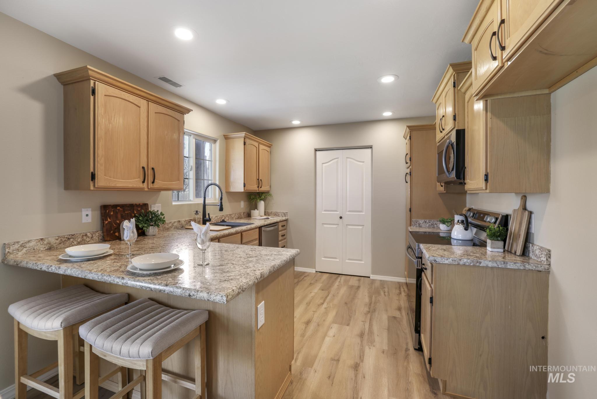 Kitchen with stainless steel appliances, a peninsula, a breakfast bar, light brown cabinets, and light wood finished floors