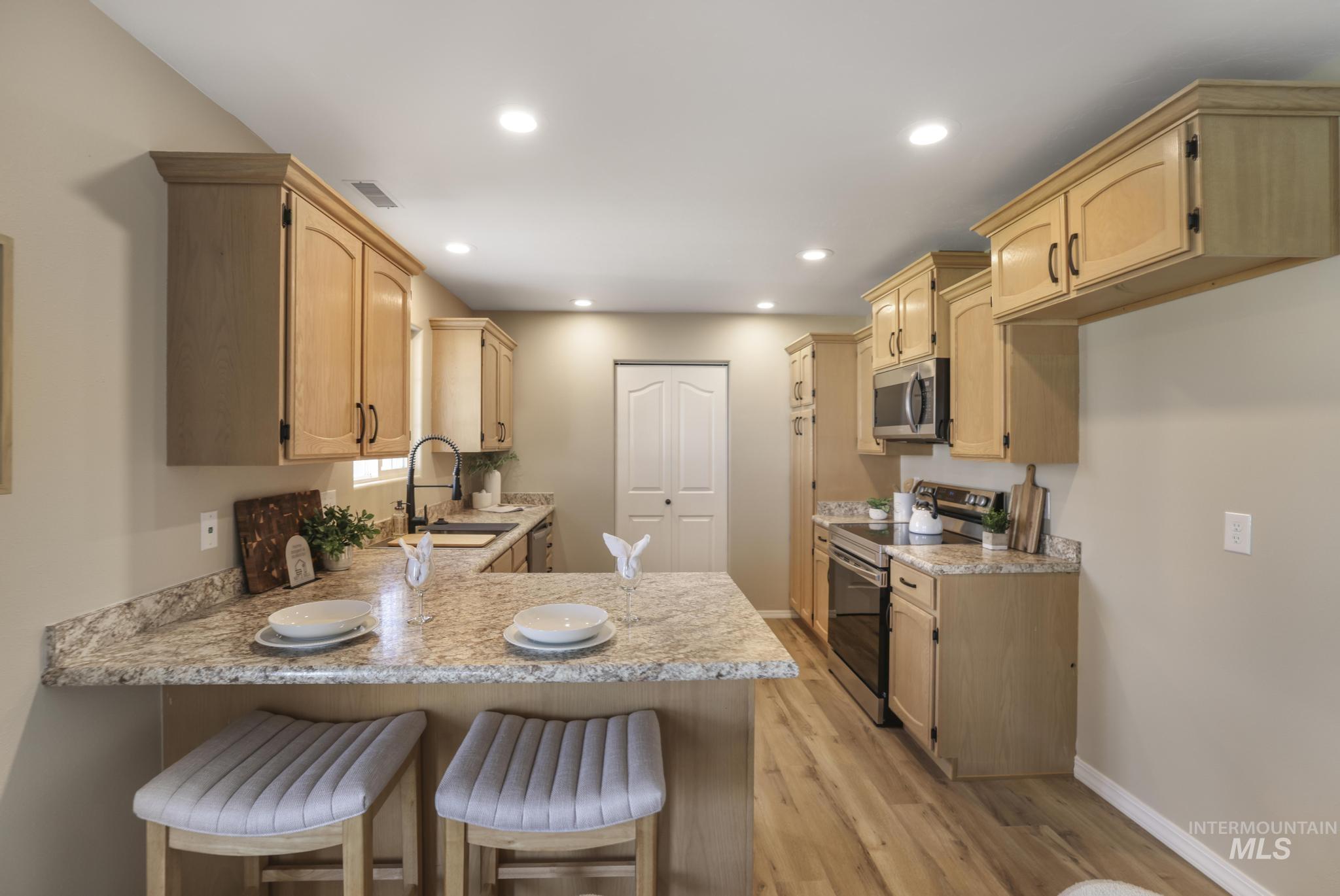 Kitchen featuring a kitchen breakfast bar, a peninsula, light brown cabinets, stainless steel appliances, and recessed lighting