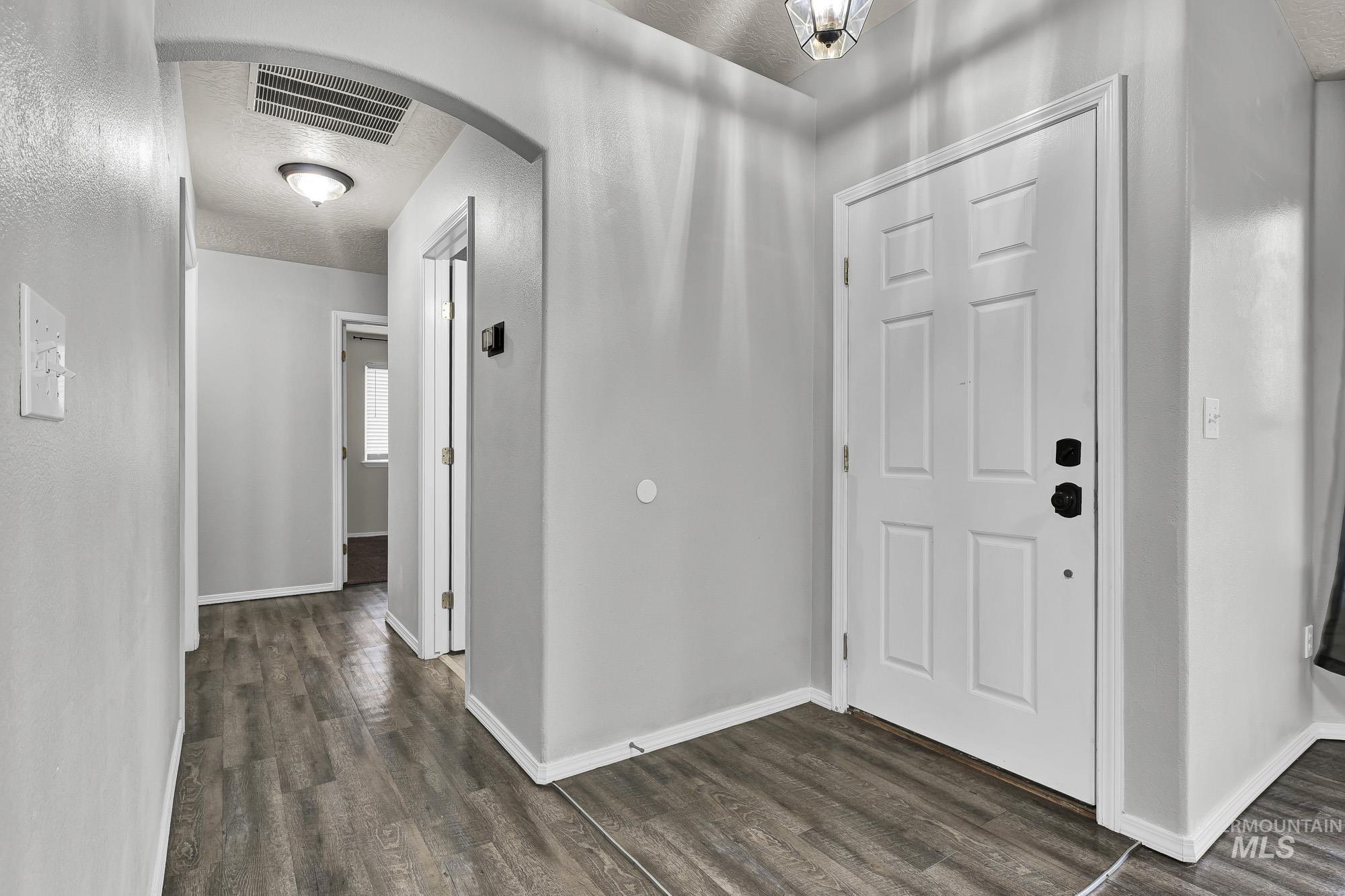 Foyer featuring arched walkways, dark wood-type flooring, and a textured ceiling