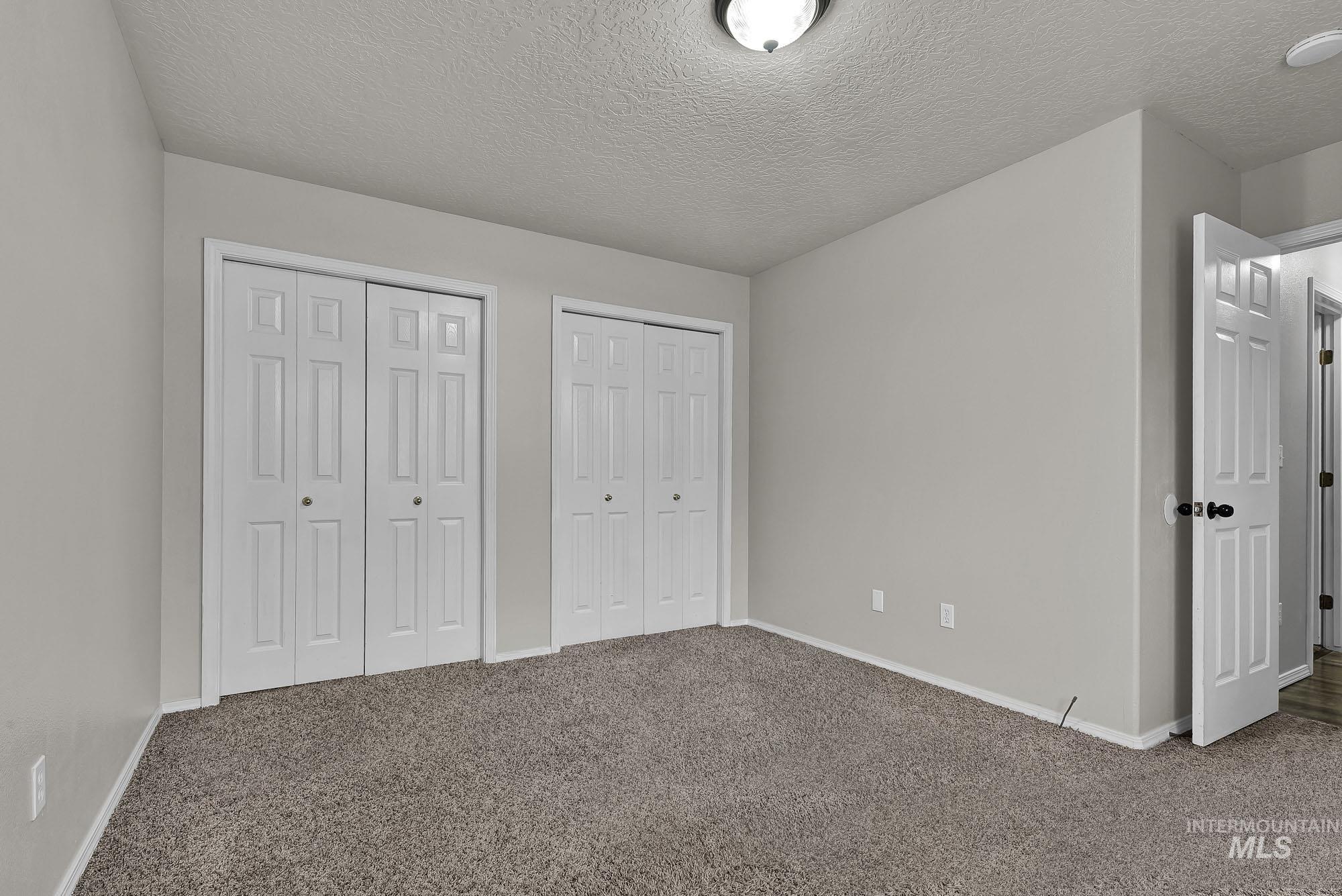 Unfurnished bedroom featuring two closets, carpet floors, and a textured ceiling