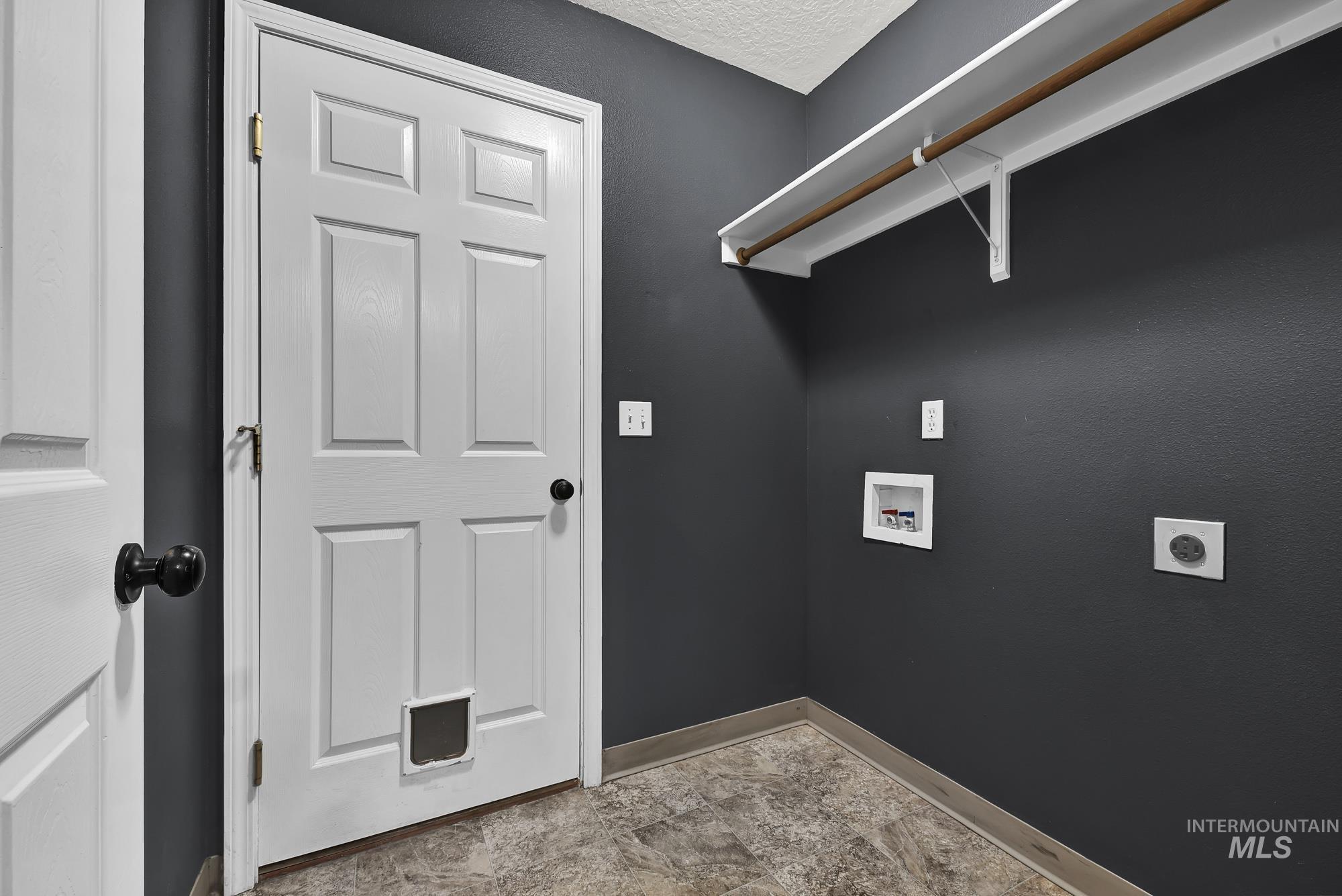 Laundry area with hookup for an electric dryer, washer hookup, stone finish floors, and a textured ceiling