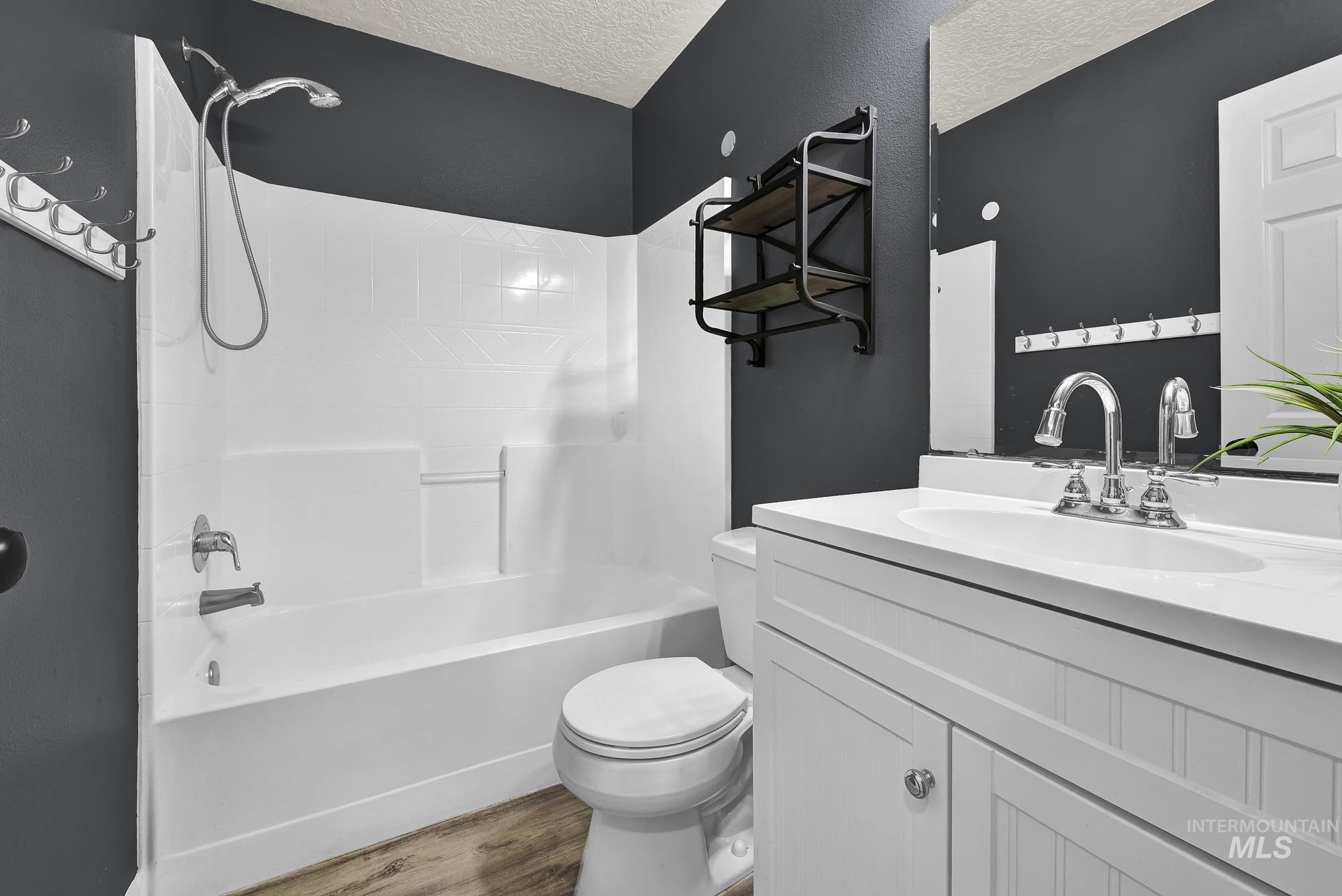 Full bathroom with a textured ceiling, vanity, shower / washtub combination, and light wood-style floors