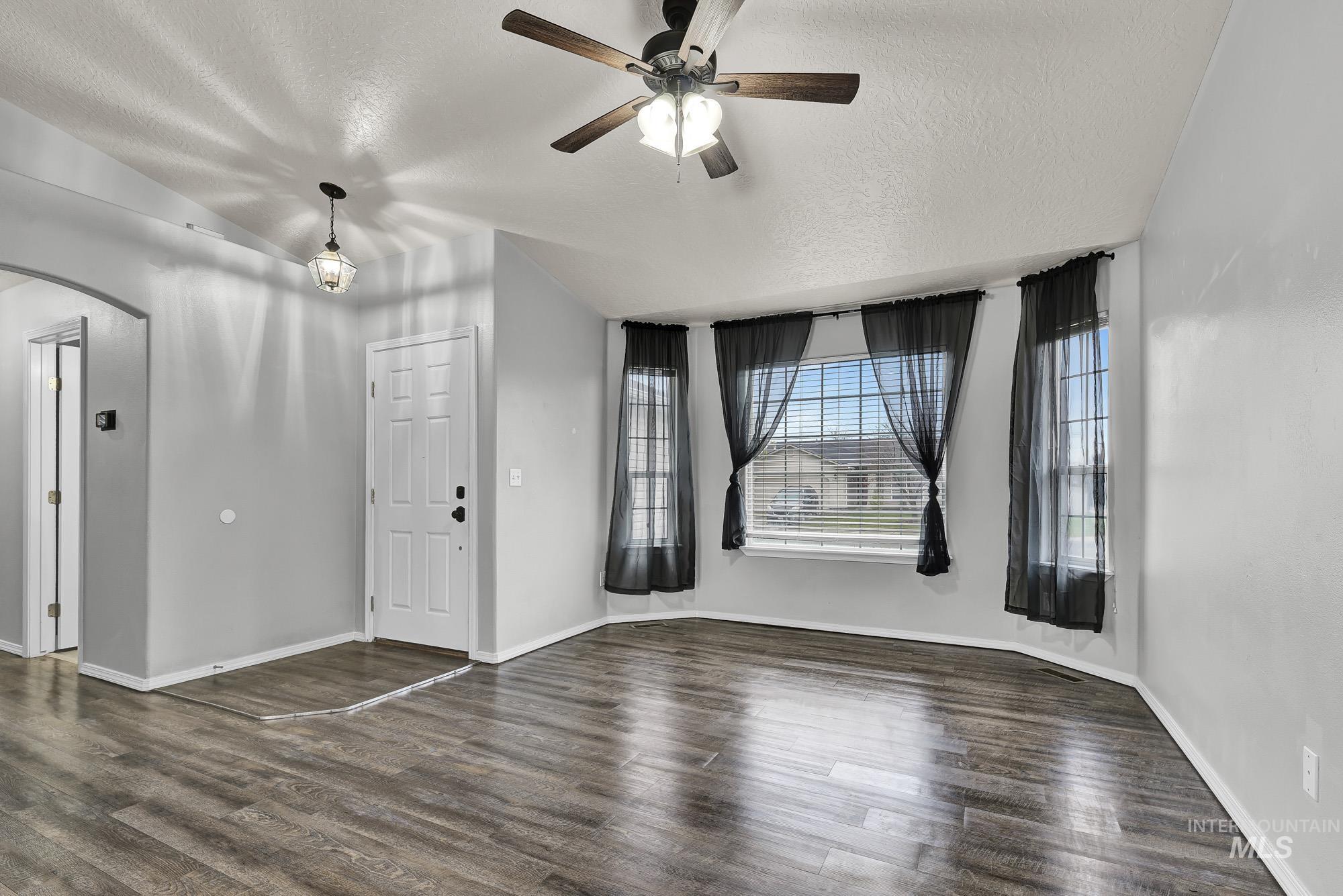 Unfurnished living room with a textured ceiling, arched walkways, dark wood-type flooring, and a ceiling fan