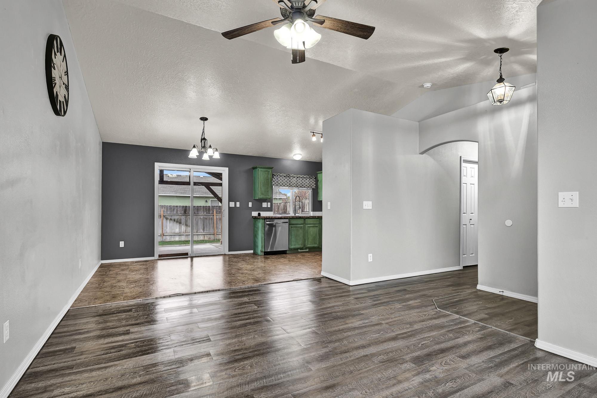 Unfurnished living room featuring dark wood-style floors, a textured ceiling, a ceiling fan, a chandelier, and lofted ceiling