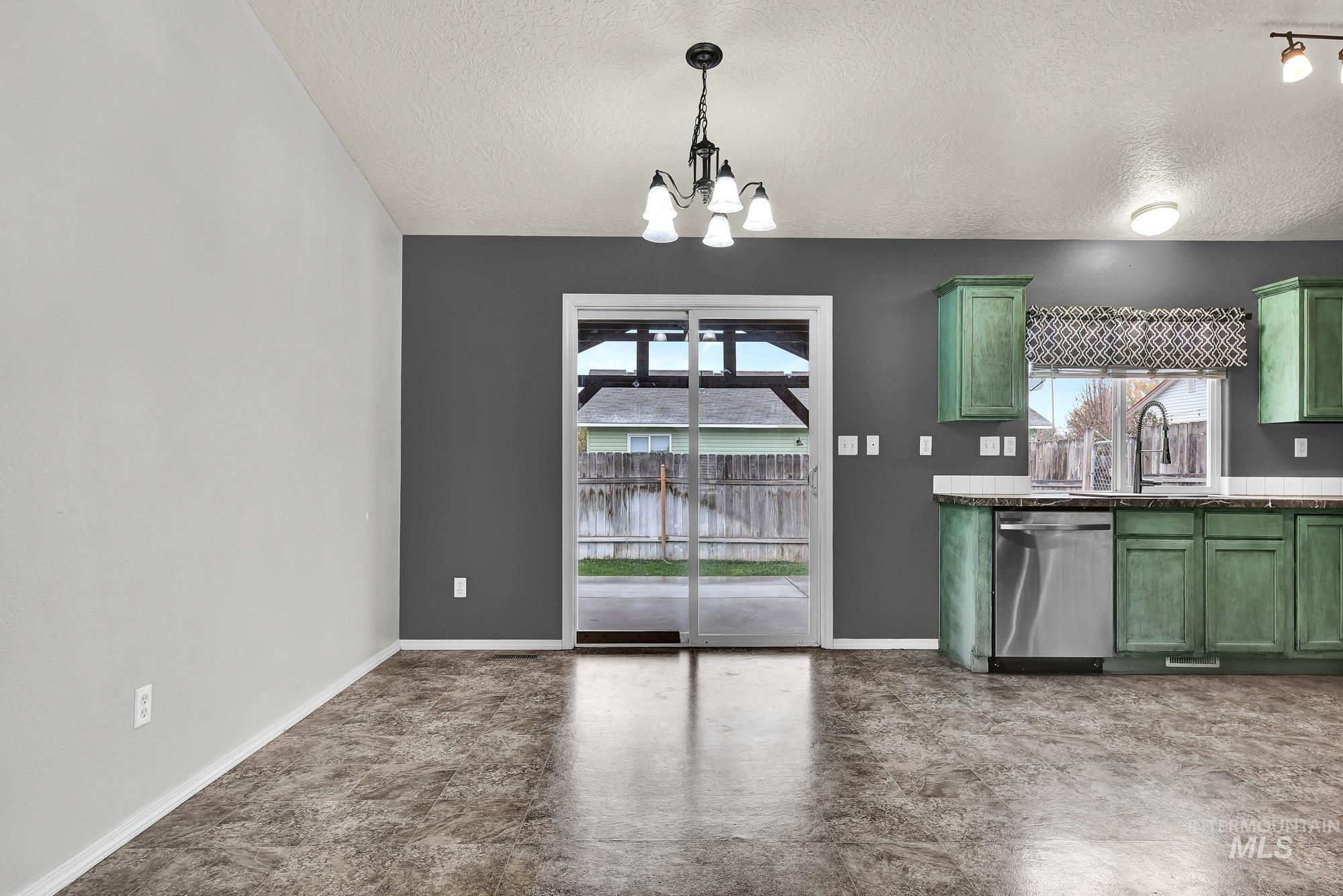 Kitchen featuring green cabinets, stainless steel dishwasher, pendant lighting, a textured ceiling, and a chandelier
