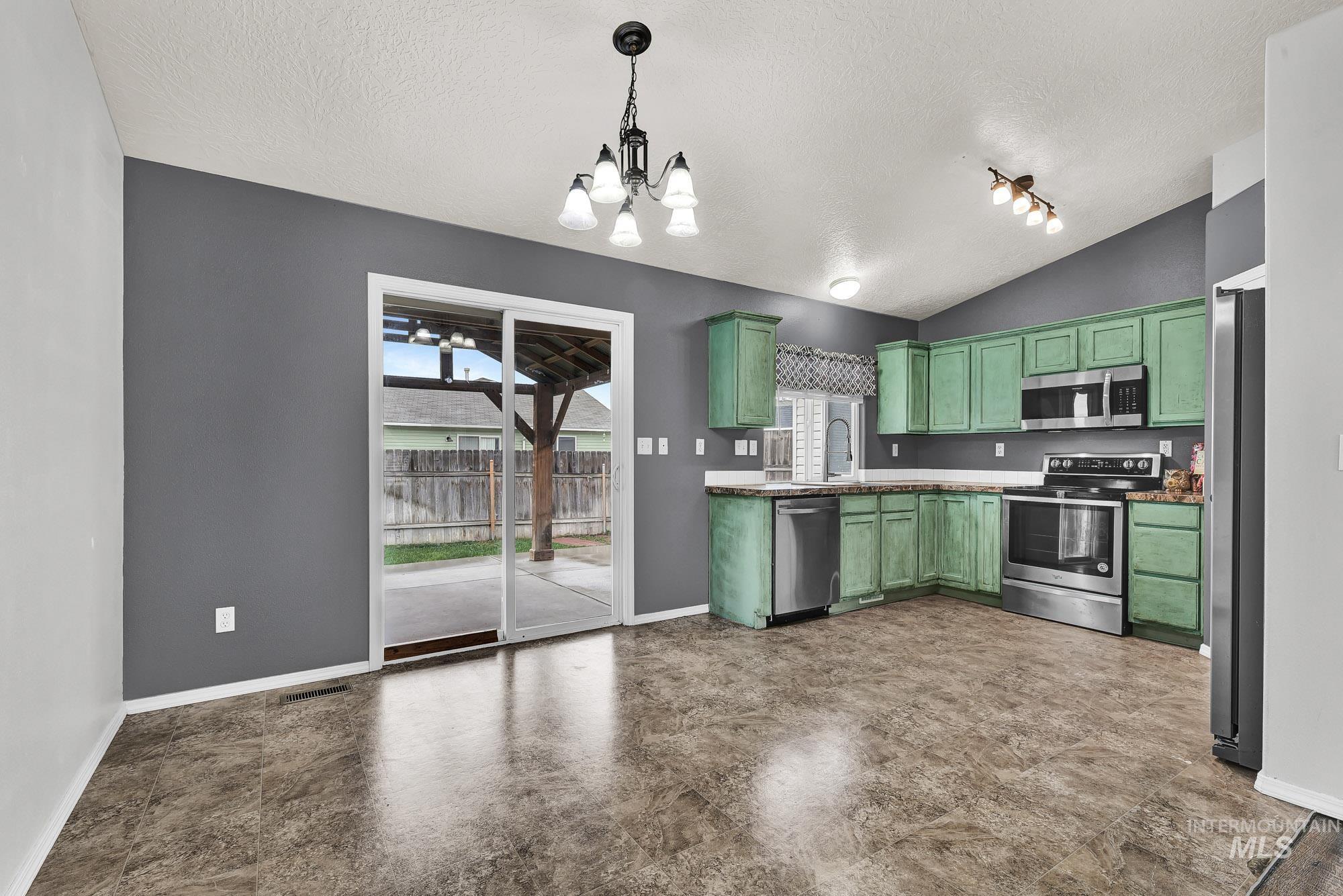 Kitchen featuring green cabinets, stainless steel appliances, a chandelier, vaulted ceiling, and a textured ceiling
