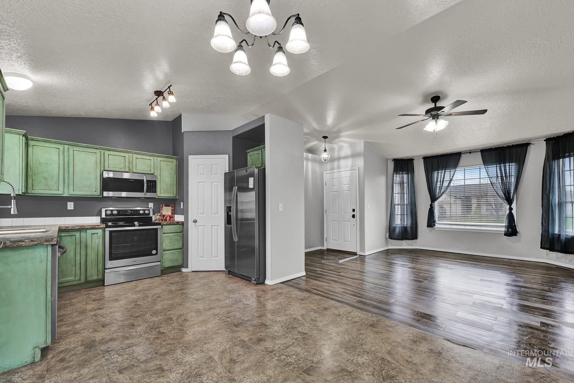 Kitchen featuring a textured ceiling, stainless steel appliances, green cabinets, a chandelier, and open floor plan