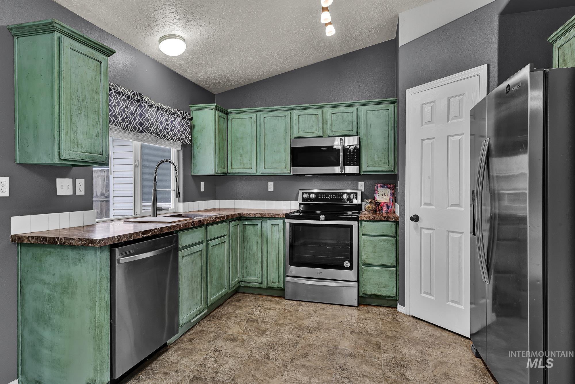 Kitchen featuring green cabinets, stainless steel appliances, a textured ceiling, and lofted ceiling