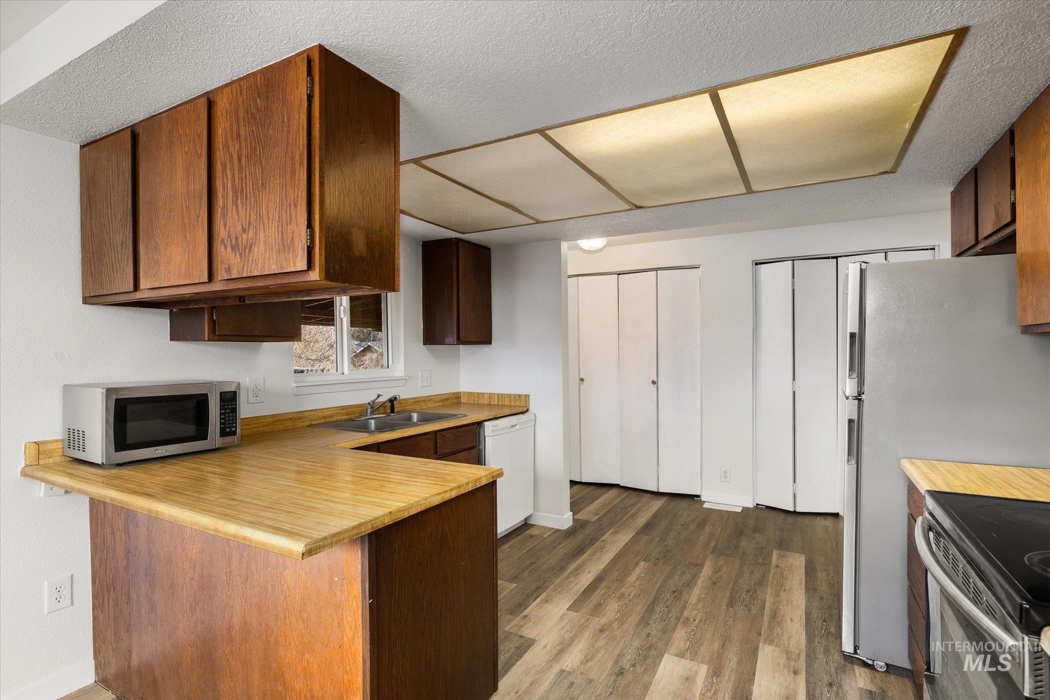 Kitchen featuring a peninsula, dark wood-type flooring, stainless steel appliances, a textured ceiling, and a kitchen bar