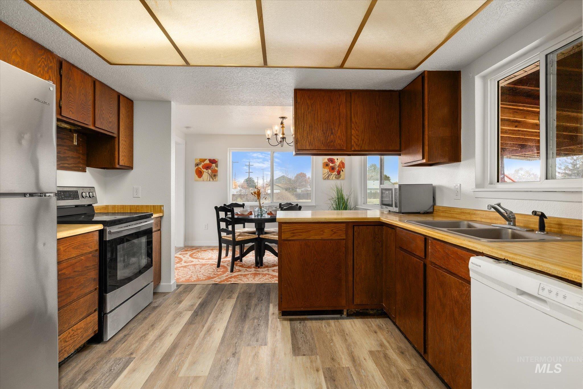 Kitchen featuring appliances with stainless steel finishes, light countertops, a chandelier, light wood-type flooring, and a textured ceiling