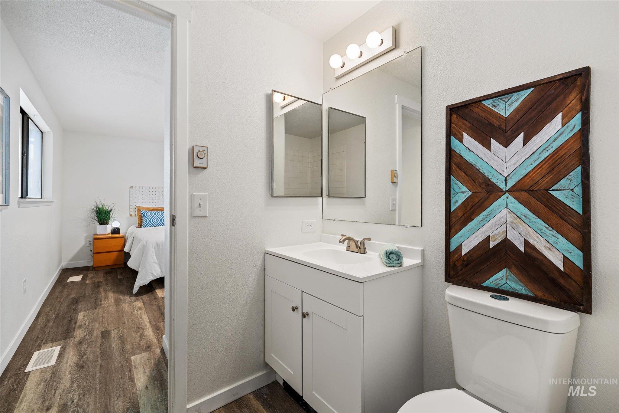 Ensuite bathroom with dark wood-type flooring, vanity, and a textured wall