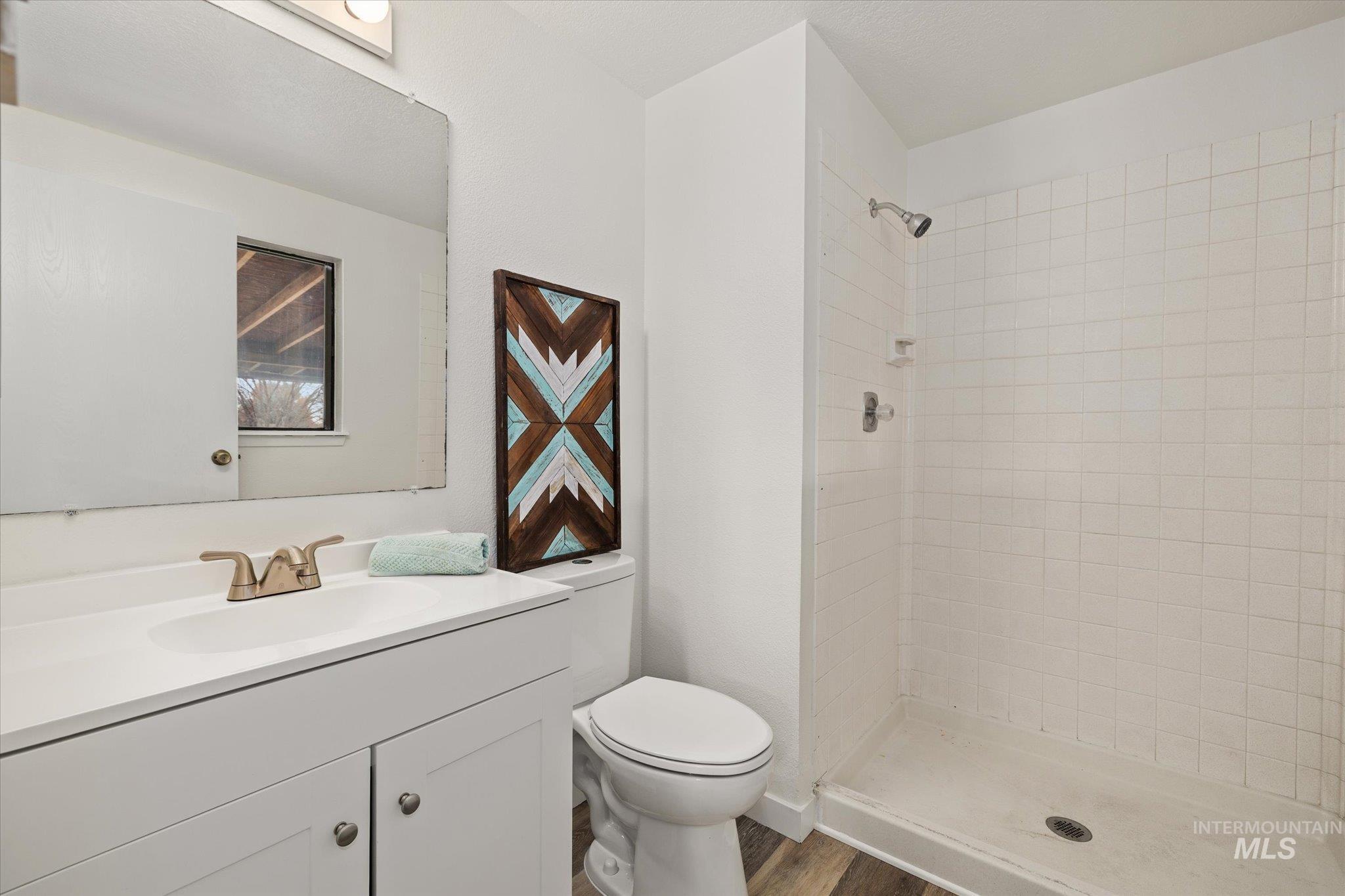 Full bath featuring vanity, a stall shower, and dark wood-style flooring