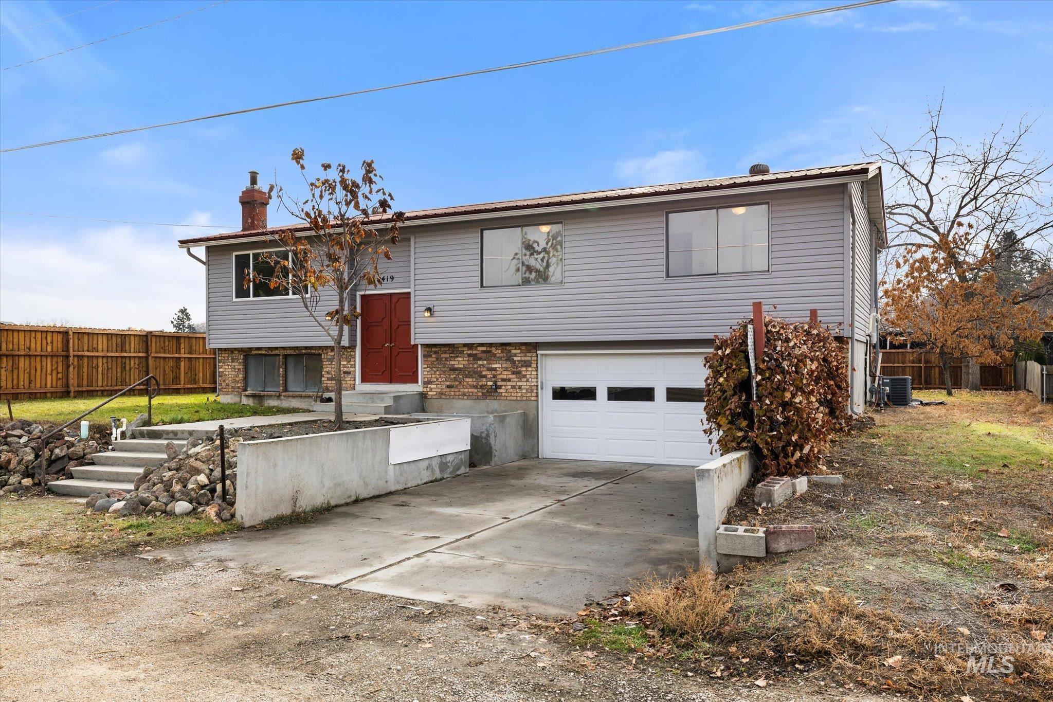 Raised ranch featuring driveway, brick siding, a chimney, and a garage