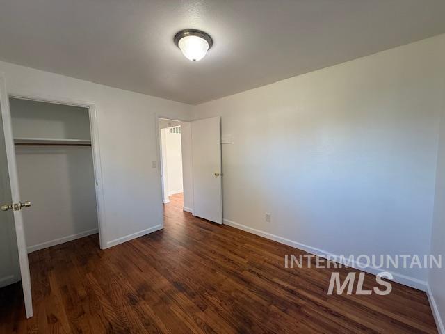 Unfurnished bedroom featuring dark wood-type flooring and a closet