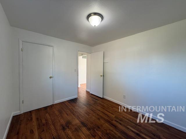 Unfurnished bedroom featuring dark wood-type flooring and baseboards