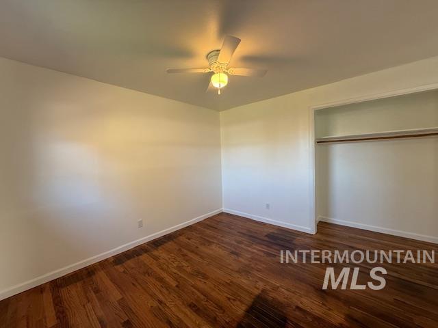 Unfurnished bedroom featuring dark wood-style flooring, a ceiling fan, and a closet