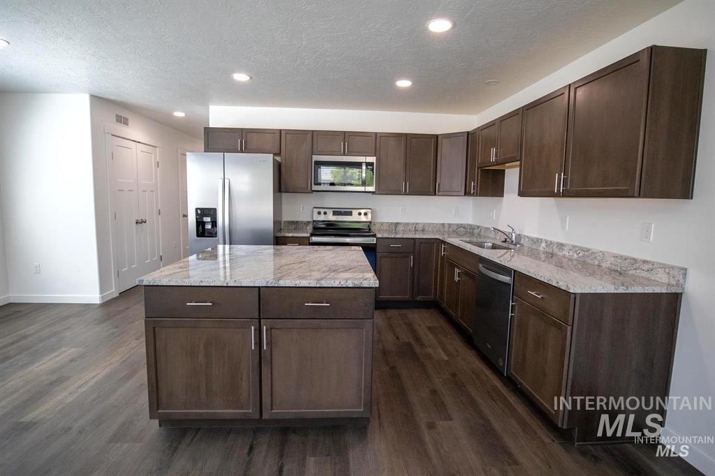 Kitchen with dark brown cabinets, appliances with stainless steel finishes, a center island, dark wood-style flooring, and a textured ceiling