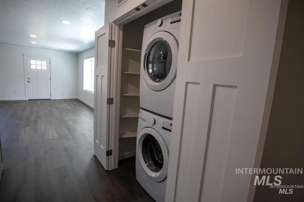 Laundry room featuring dark wood finished floors, stacked washing machine and dryer, a textured ceiling, and recessed lighting