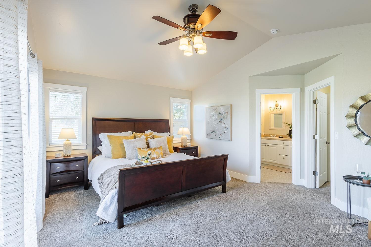 Bedroom with multiple windows, light carpet, vaulted ceiling, a ceiling fan, and ensuite bathroom