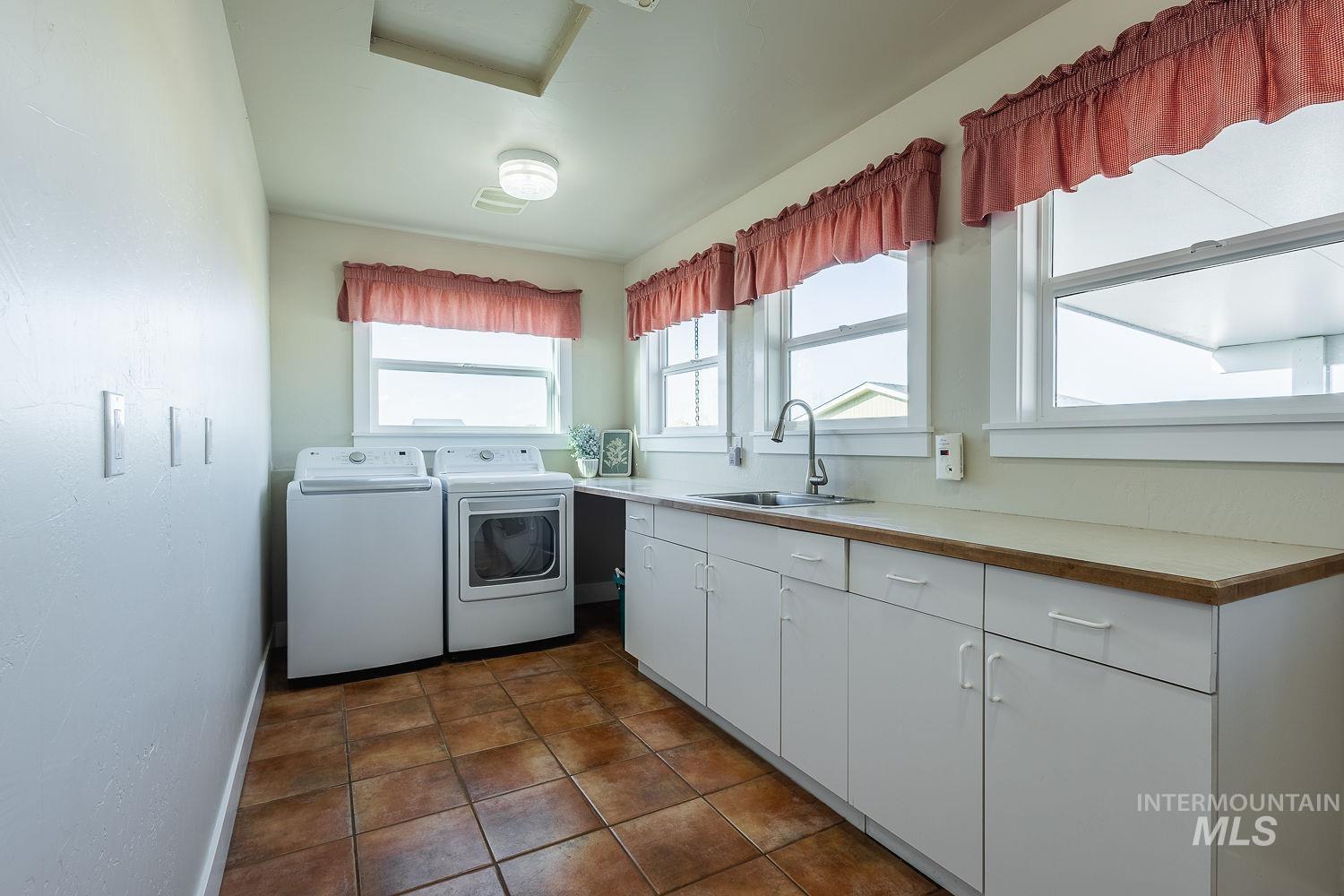 Laundry area with washing machine and clothes dryer, dark tile patterned floors, and cabinet space