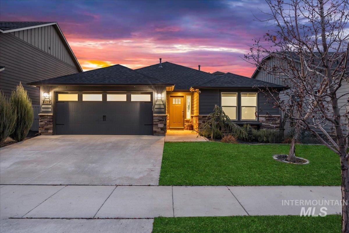 View of front of home featuring stone siding, a front lawn, a shingled roof, driveway, and a garage