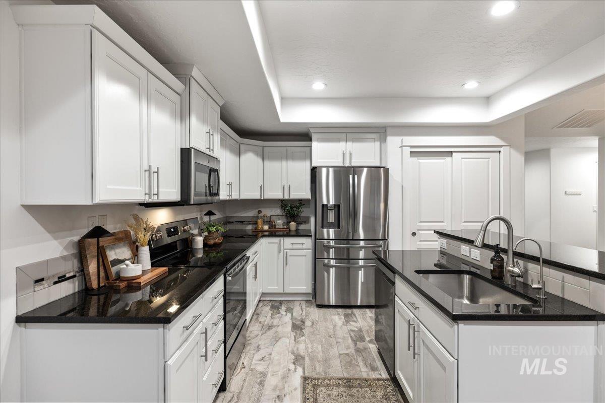 Kitchen with appliances with stainless steel finishes, a tray ceiling, white cabinets, recessed lighting, and dark stone countertops
