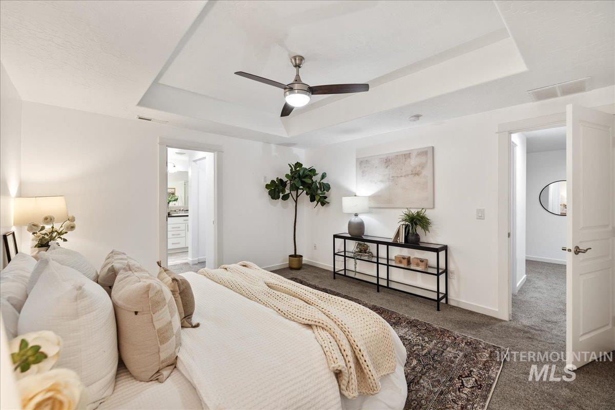 Bedroom featuring a tray ceiling, carpet flooring, ceiling fan, and ensuite bathroom