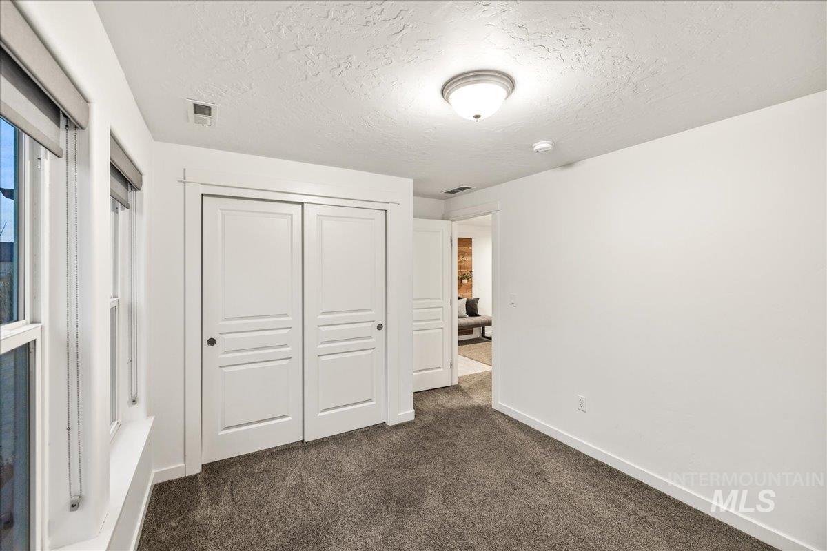 Unfurnished bedroom featuring dark colored carpet, a closet, and a textured ceiling