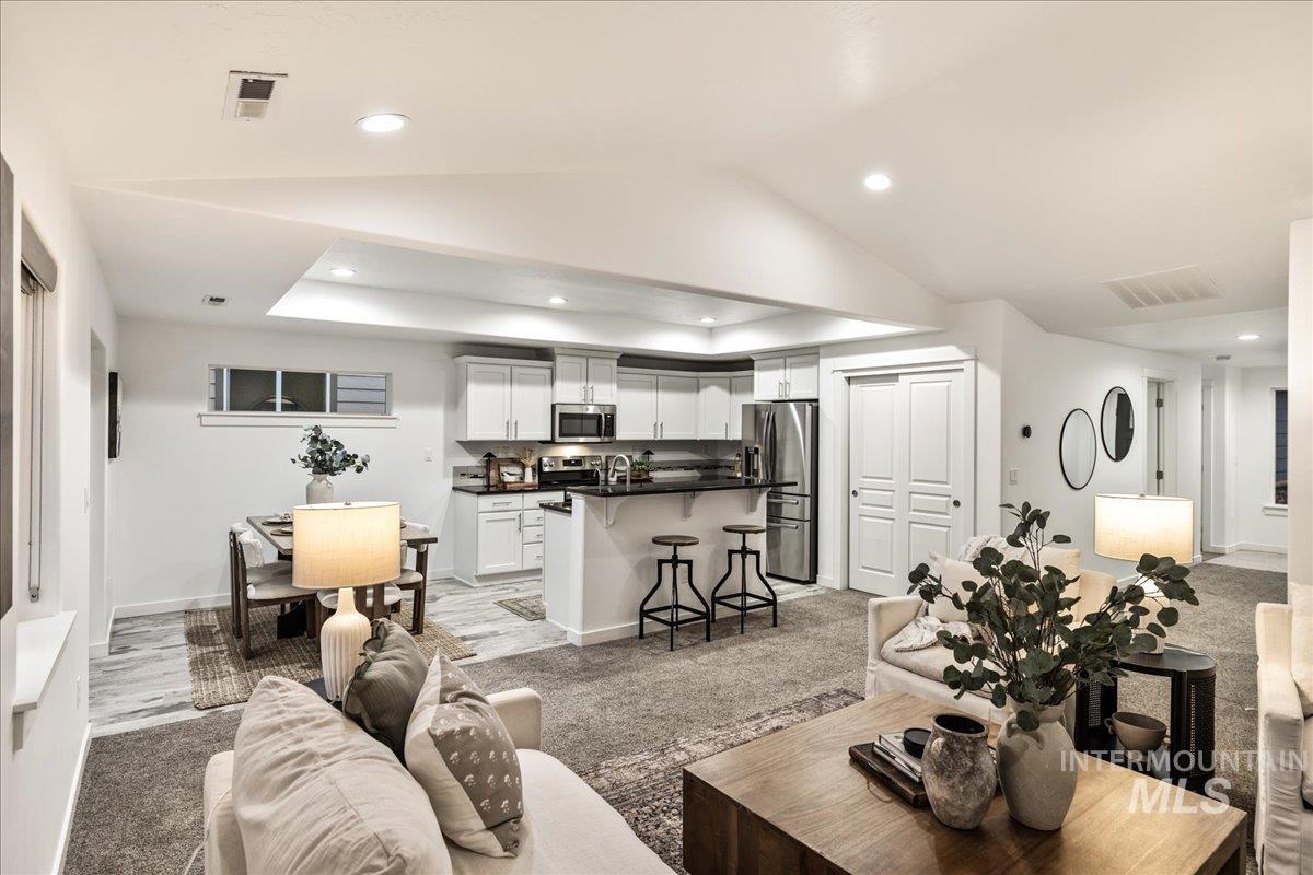 Living area with light colored carpet, recessed lighting, vaulted ceiling, and a raised ceiling