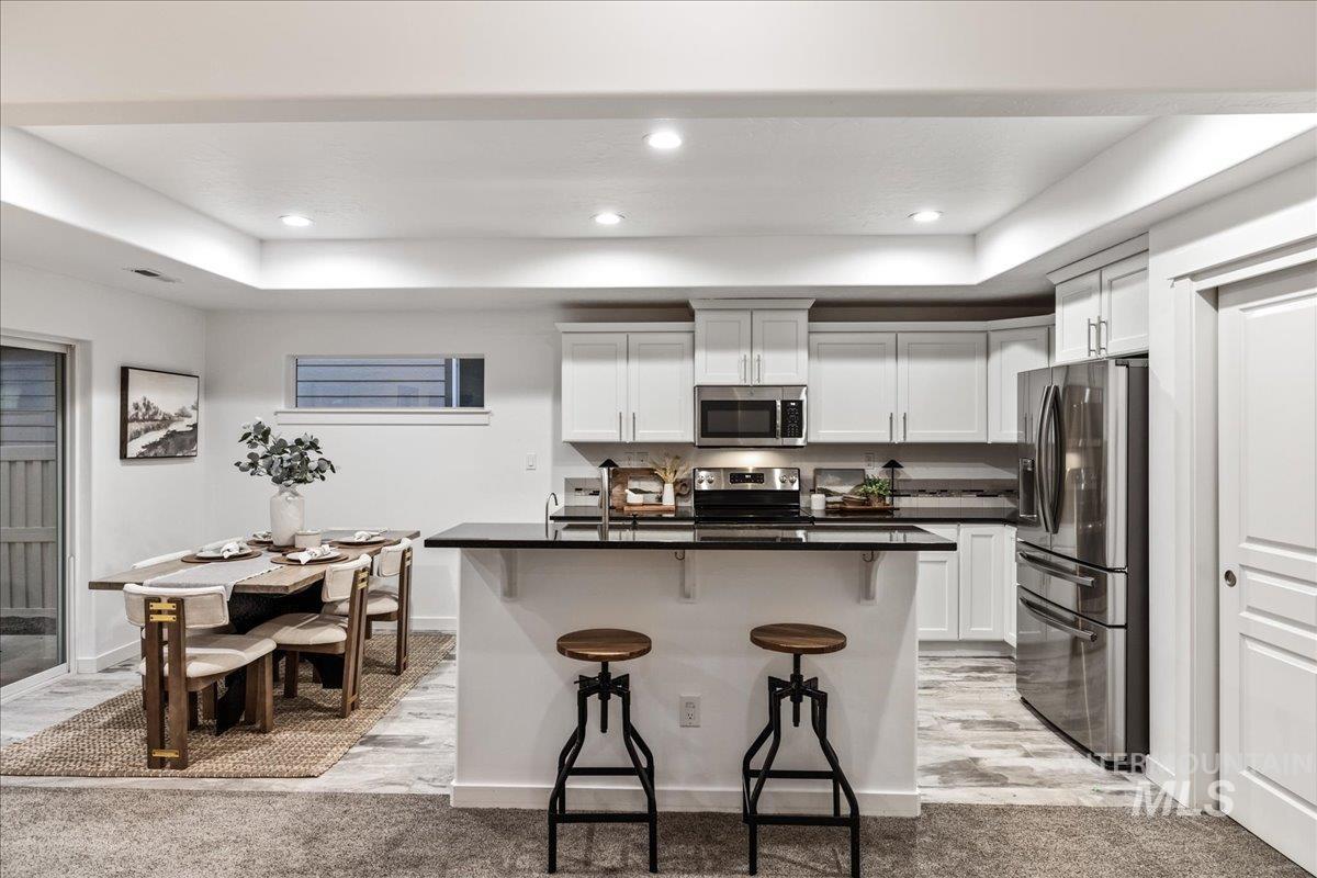 Kitchen featuring stainless steel appliances, a breakfast bar, white cabinetry, a tray ceiling, and recessed lighting