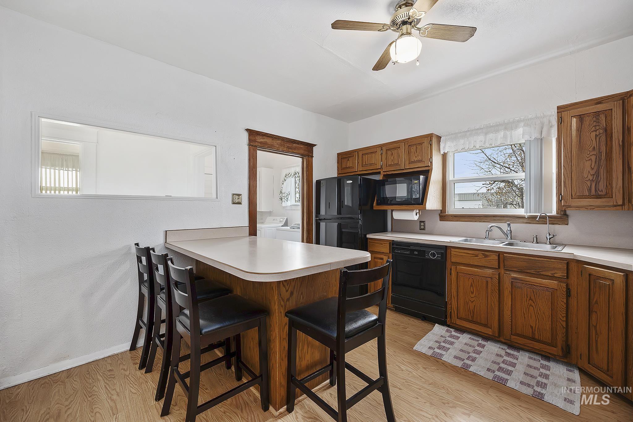 Kitchen with a kitchen breakfast bar, brown cabinets, light wood-style flooring, a peninsula, and black appliances