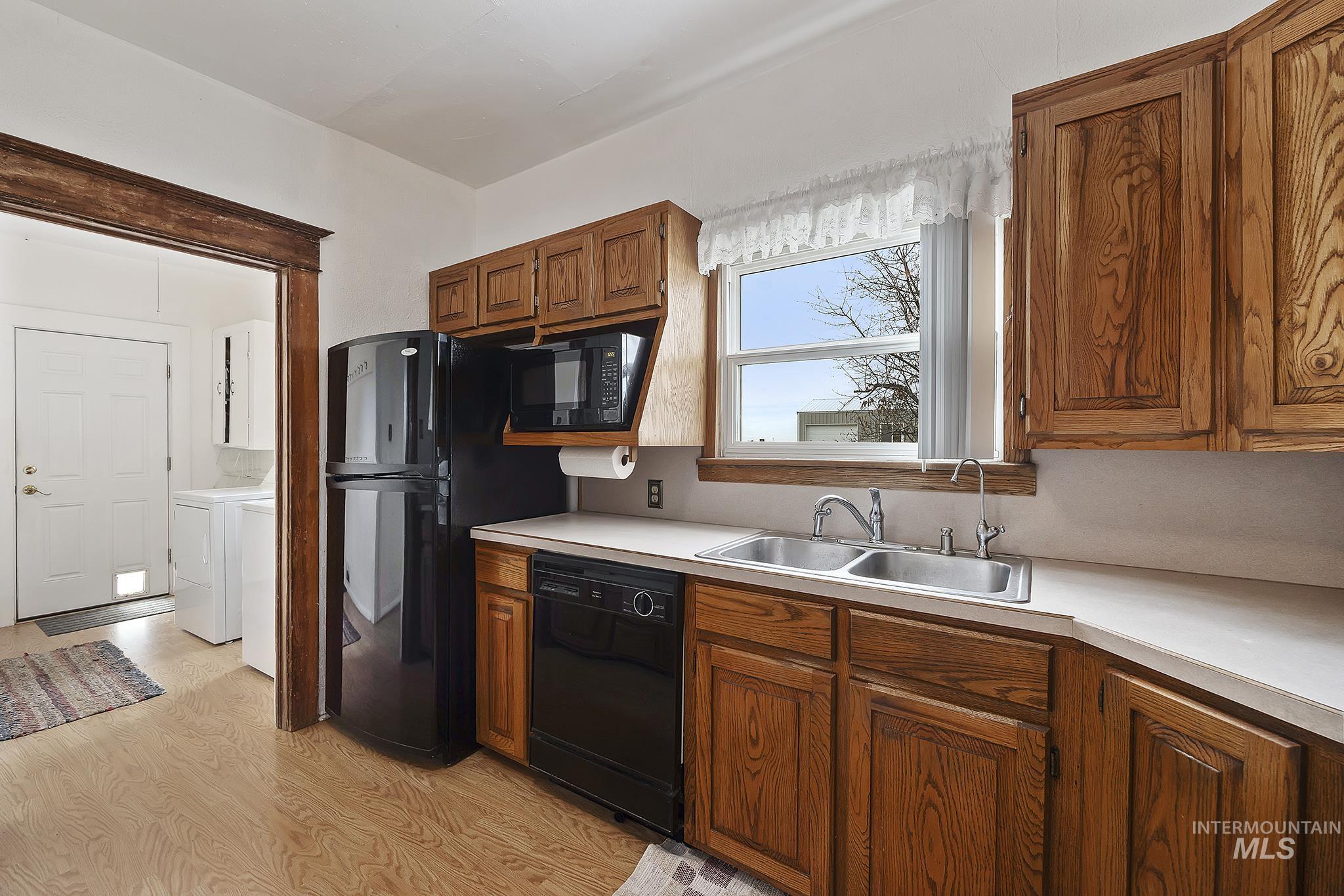 Kitchen with light wood-type flooring, black appliances, light countertops, brown cabinetry, and independent washer and dryer