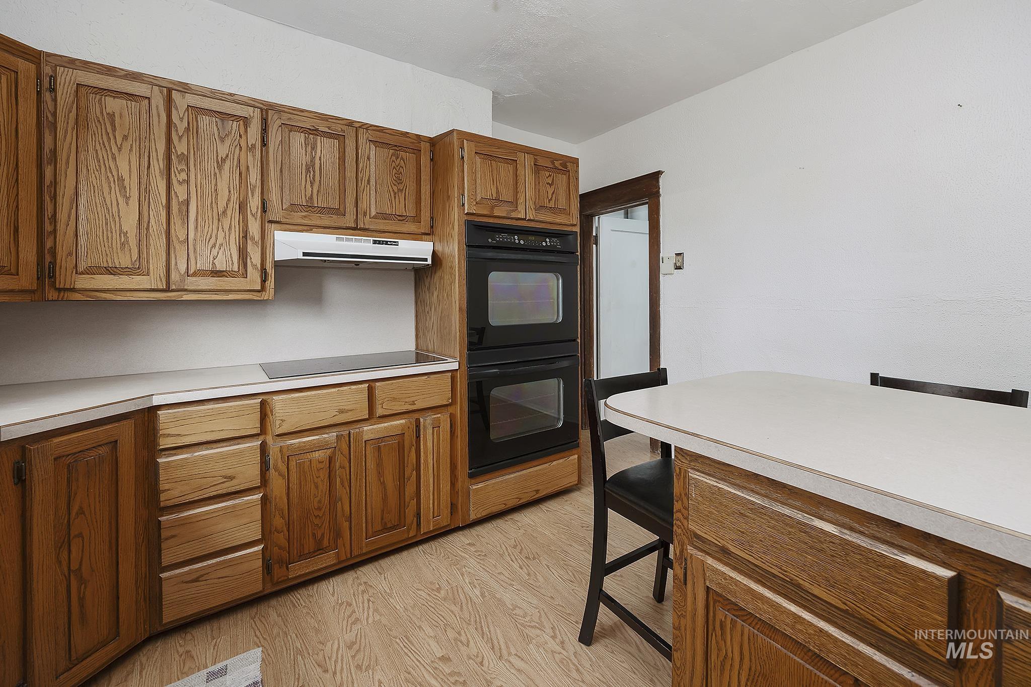 Kitchen with light countertops, brown cabinets, light wood finished floors, black appliances, and under cabinet range hood