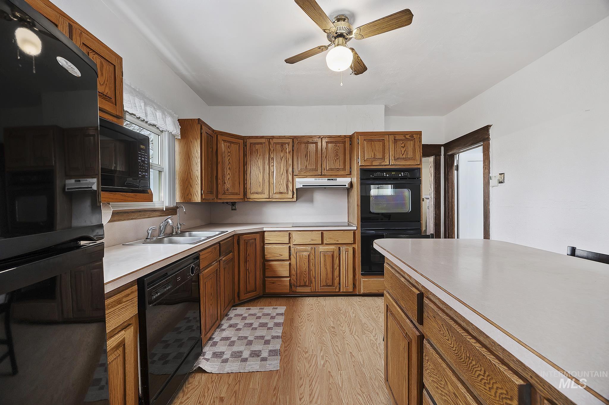 Kitchen featuring light countertops, light wood-style flooring, black appliances, and brown cabinets