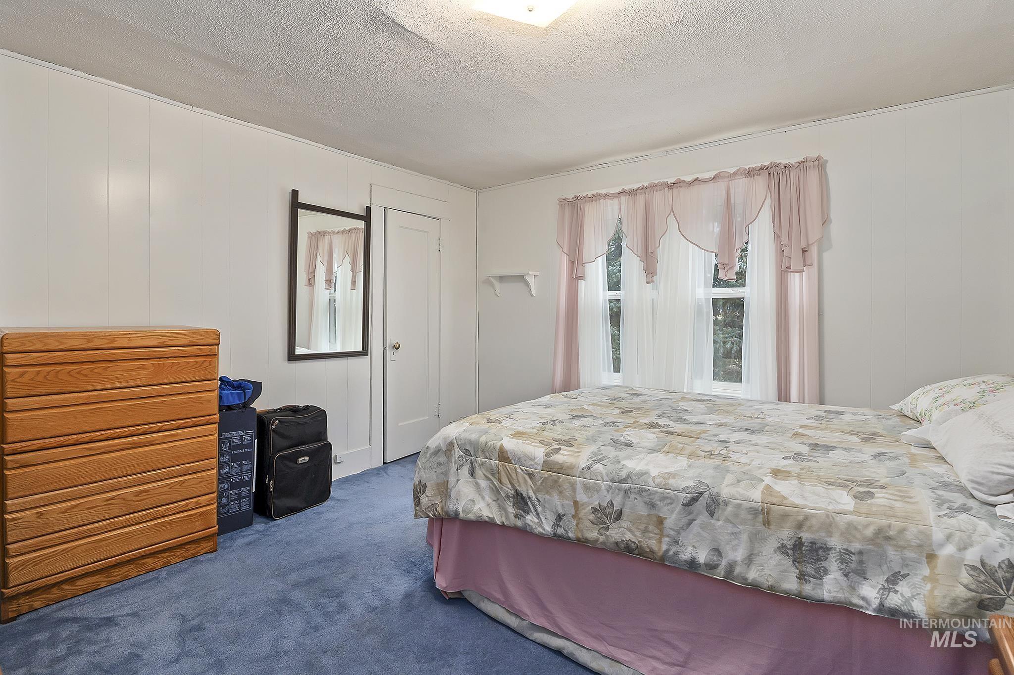 Carpeted bedroom featuring a textured ceiling and wooden walls